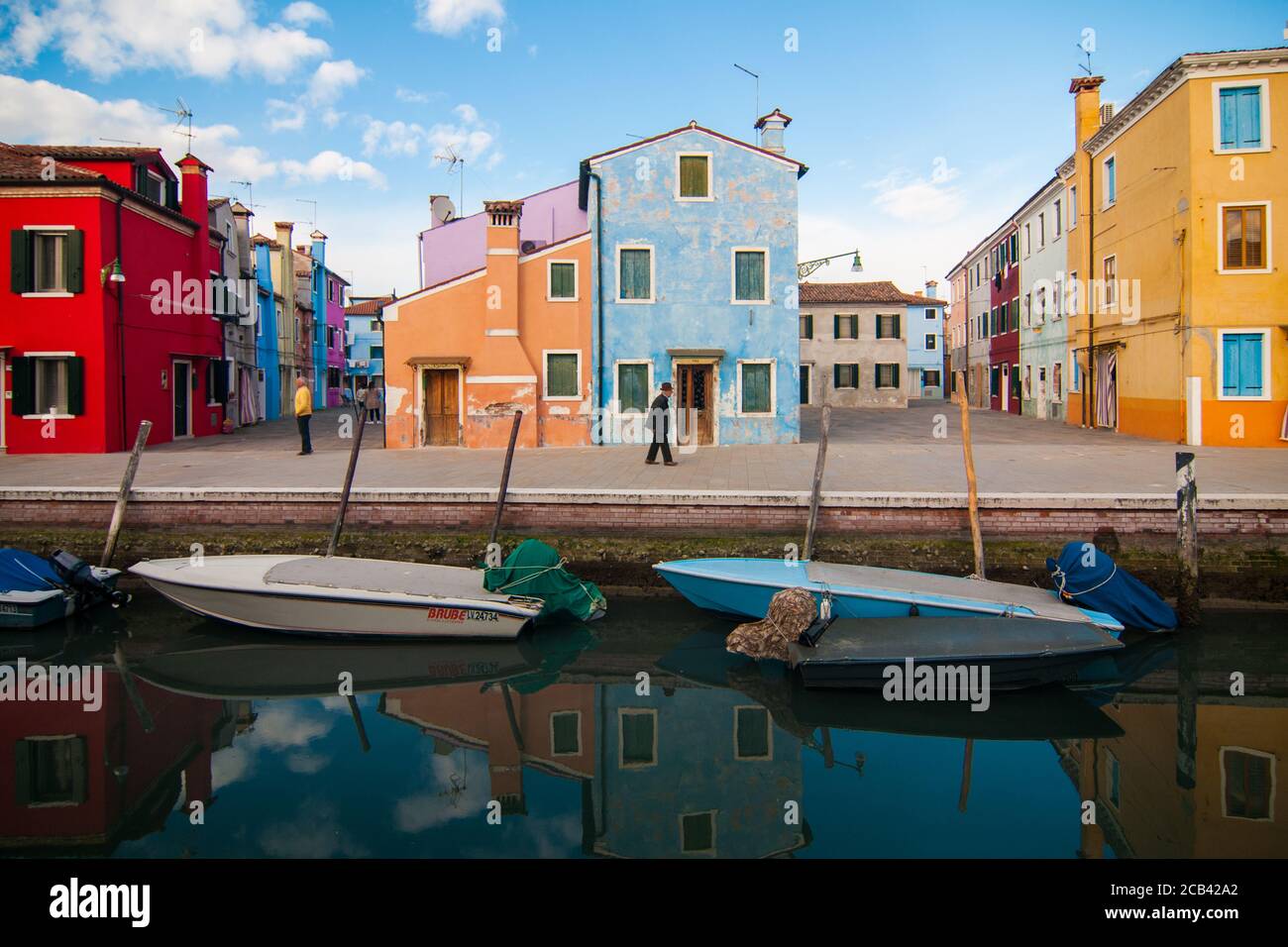 BURANO, ITALIEN - 9. MÄRZ 2017: Typische bunte Häuser der Insel Burano spiegeln sich auf einem venezianischen Kanal mit zwei Booten Stockfoto