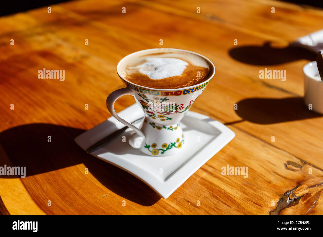 Tasse Kaffee mit Milchschaum. Serviert in einer wunderschön verzierten Tasse. Im Sonnenlicht gebadet. Stockfoto