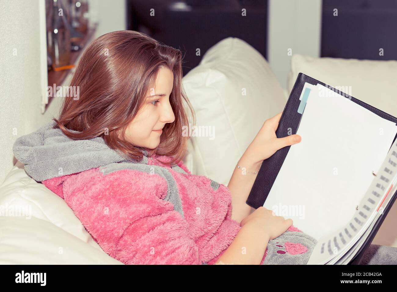 Seitenansicht der jungen legeren Frau im Pullover sitzend auf Sofa mit Notizblock und Lesestoff zu Hause Stockfoto