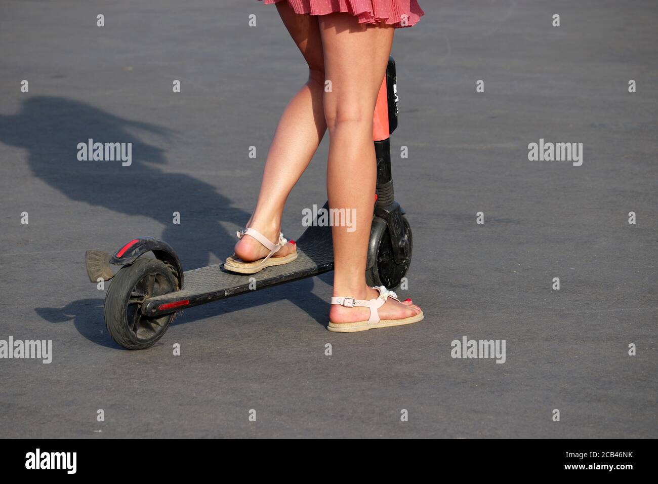 Mädchen reitet einen Elektroroller auf einer Stadtstraße, schlanke weibliche Beine auf Asphalt. Reiten E-Scooter im Sommer Stockfoto