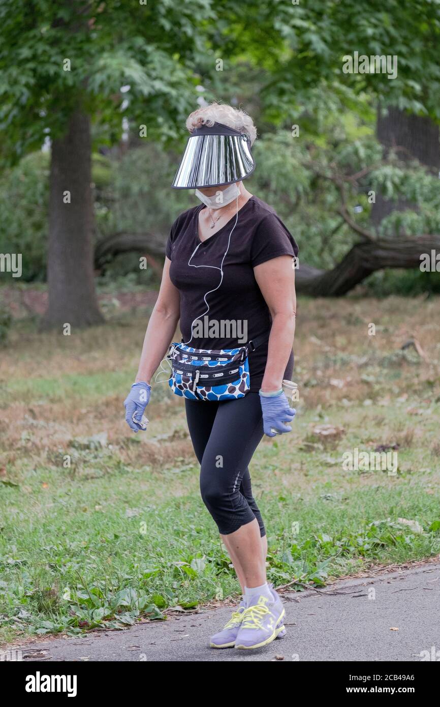 Eine Frau mittleren Alters, die mit einem Gesichtsschild unterwegs ist, um einen Übungsweg zu machen. In Flushing, Queens, New York City. Stockfoto