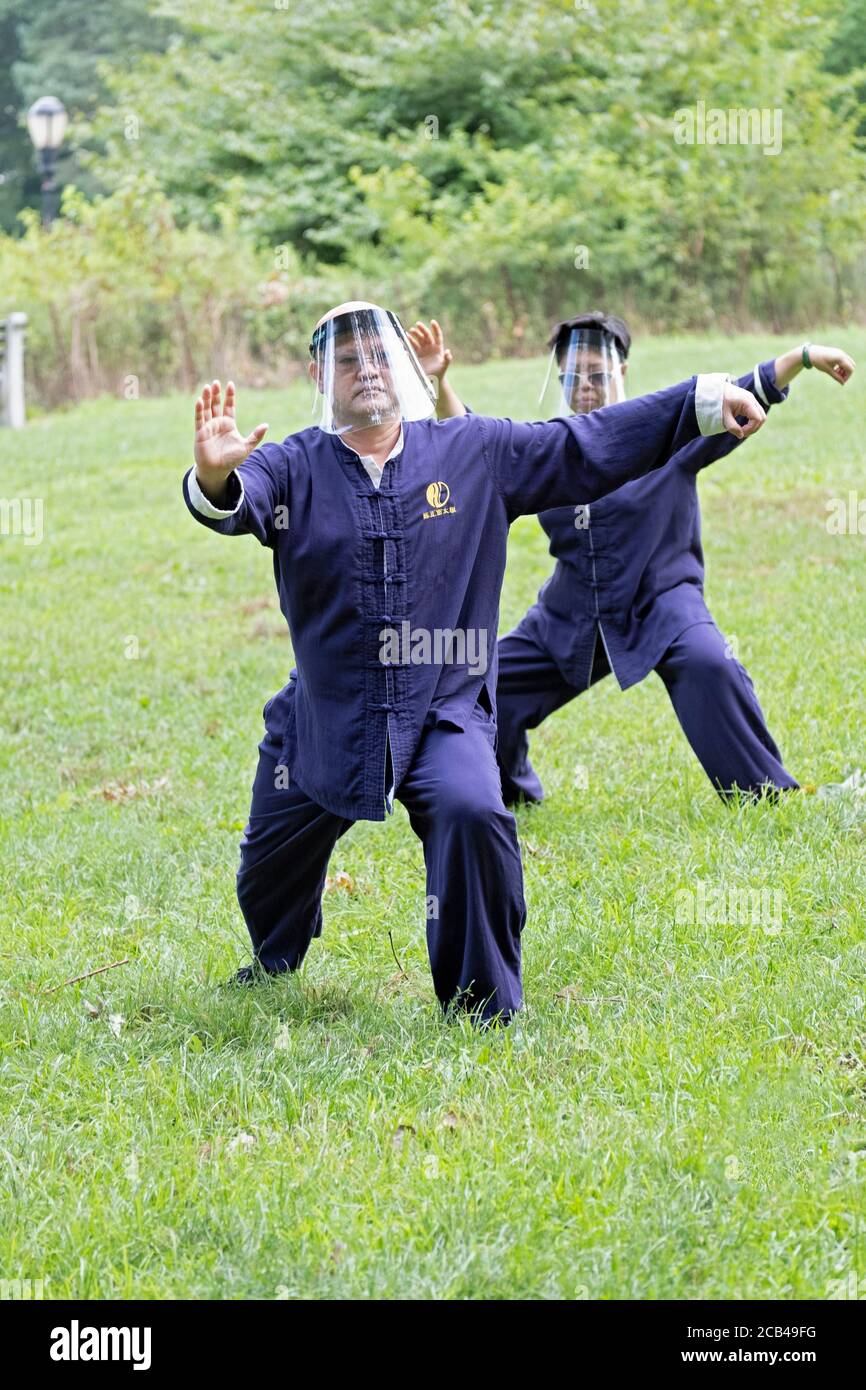 Ein asiatisch-amerikanisches Paar, das Gesichtsschilde trägt, besucht eine Tai-Chi-Klasse/Lektion im Kissena Park in Flushing, New York City. Stockfoto