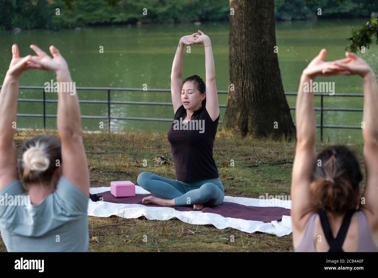 Eine chinesisch-amerikanische Yogalehrerin und 2 weibliche Schüler sitzen und halten ihre Arme und Hände zusammen. In Kissena Park, Flushing, Queens, NYC. Stockfoto