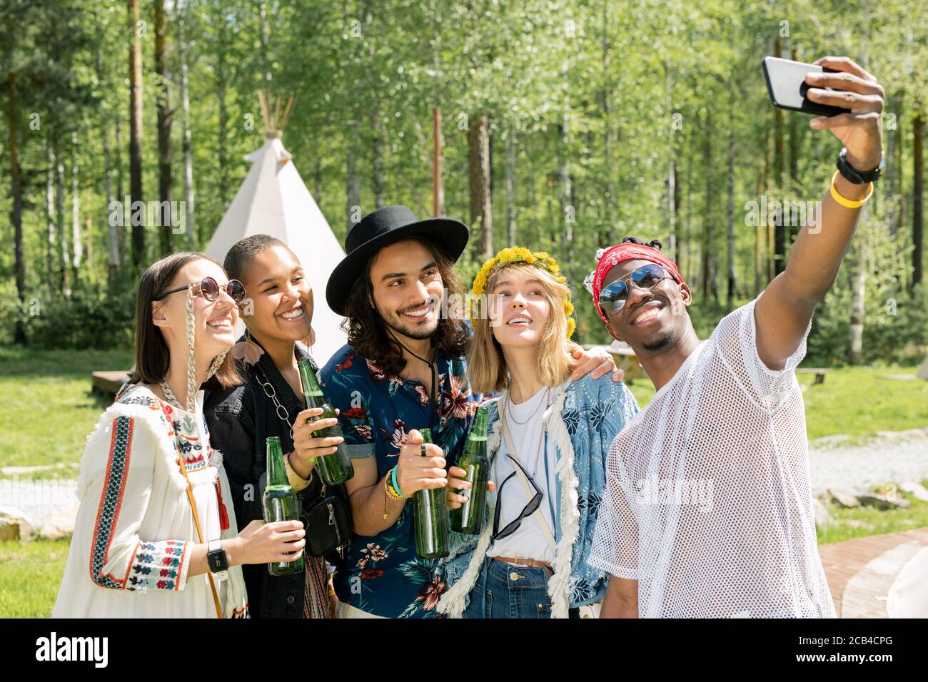 Lächelnd schöner afroamerikanischer Kerl in Sonnenbrille posiert mit besten multi-ethnischen Freunde auf dem Campingplatz beim Selfie zusammen Stockfoto