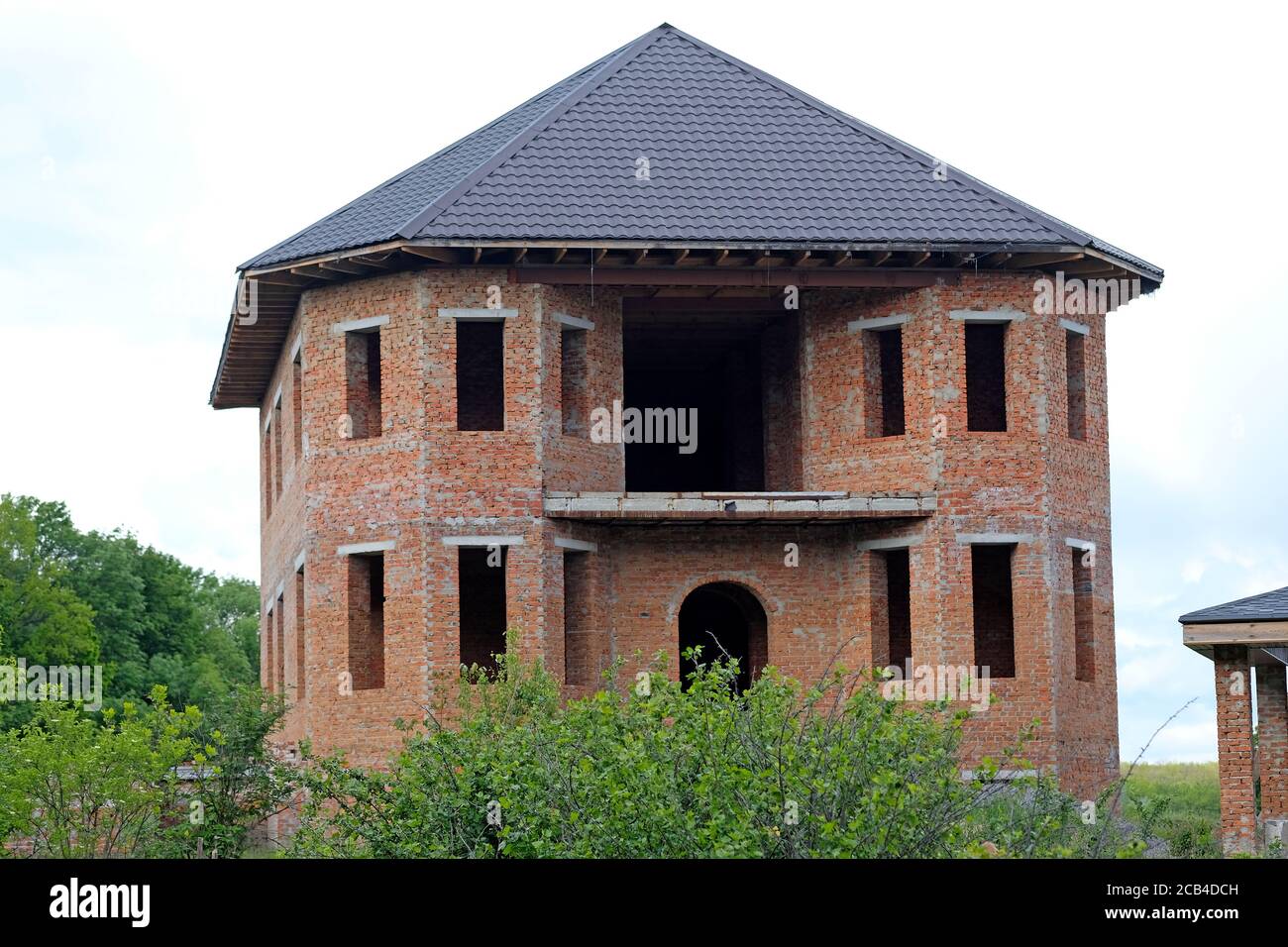 Fassade eines unfertigen zweistöckigen Hauses ohne rote Backsteinfenster. Großes Haus mit abgerundeten Ecken und einer großen Terrasse. Der Prozess des Aufbaus eines Hou Stockfoto
