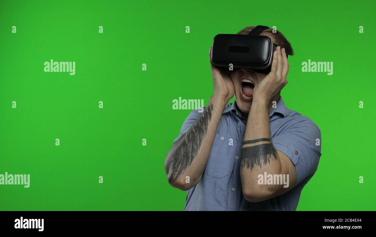 Mann mit VR-App Headset Helm zu beängstigend Simulation Spiel zu spielen. Beobachten Virtual Reality 3d 360 Video und schreit in Angst auf Chroma-Taste grünen Hintergrund im Studio. Kerl in VR-Brille, der sich umsieht Stockfoto