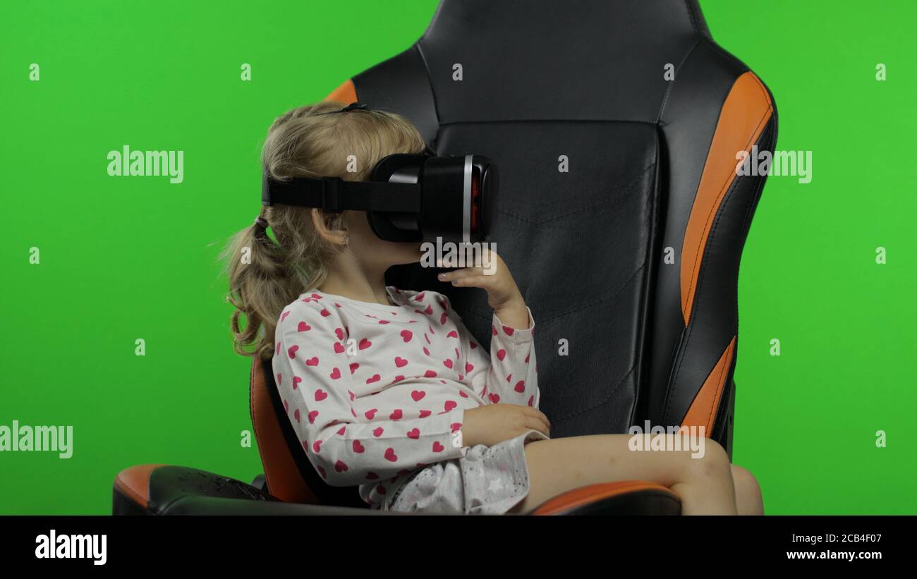 Kind teen Mädchen setzt auf VR-Headset Helm zu Simulation App-Spiel zu spielen. Virtual Reality 3d 360-Video ansehen. Chroma Key Hintergrund im Studio. Kind mit VR-Brille herumschauen sitzen auf Gamer-Stuhl Stockfoto