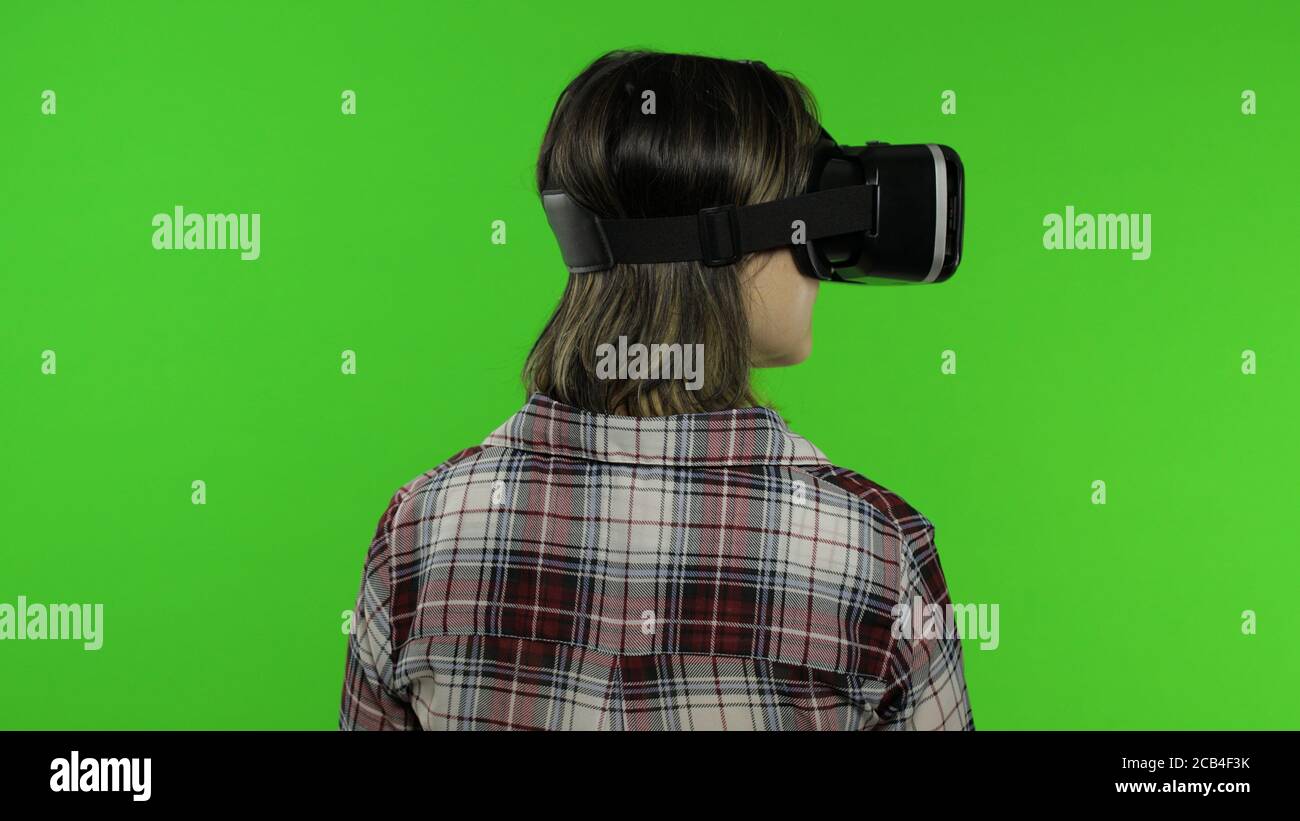 Junge Frau mit VR-App Headset Helm, um Simulationsspiel zu spielen. Virtual Reality 3d 360-Video ansehen. Isoliert auf Chroma-Taste grünen Hintergrund im Studio. Mädchen in VR-Brille, die sich umsieht, Daumen hoch Stockfoto