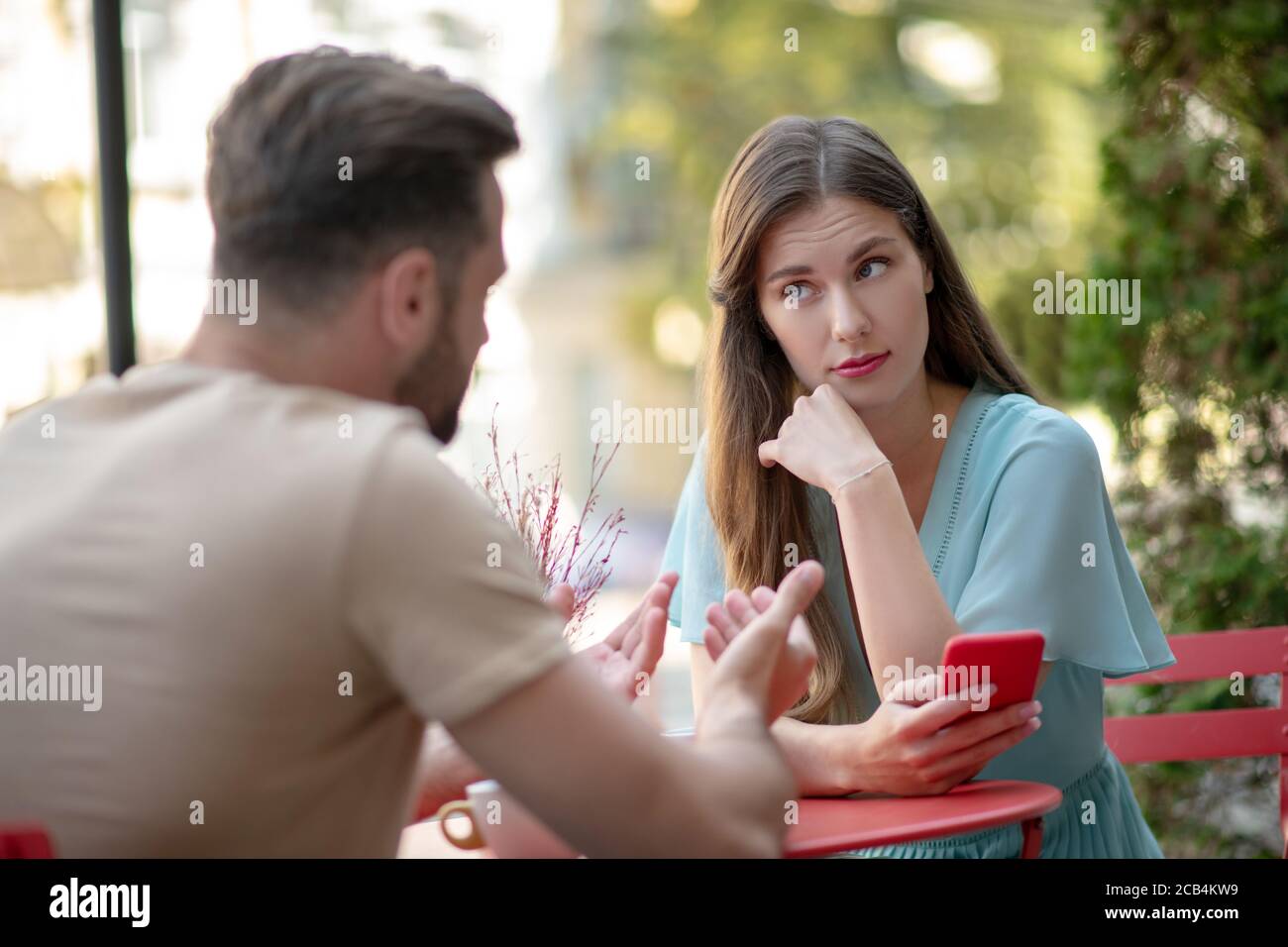 Paar mit Missverständnis im Open-Air-Café, traurige Frau hält ihr Telefon Stockfoto