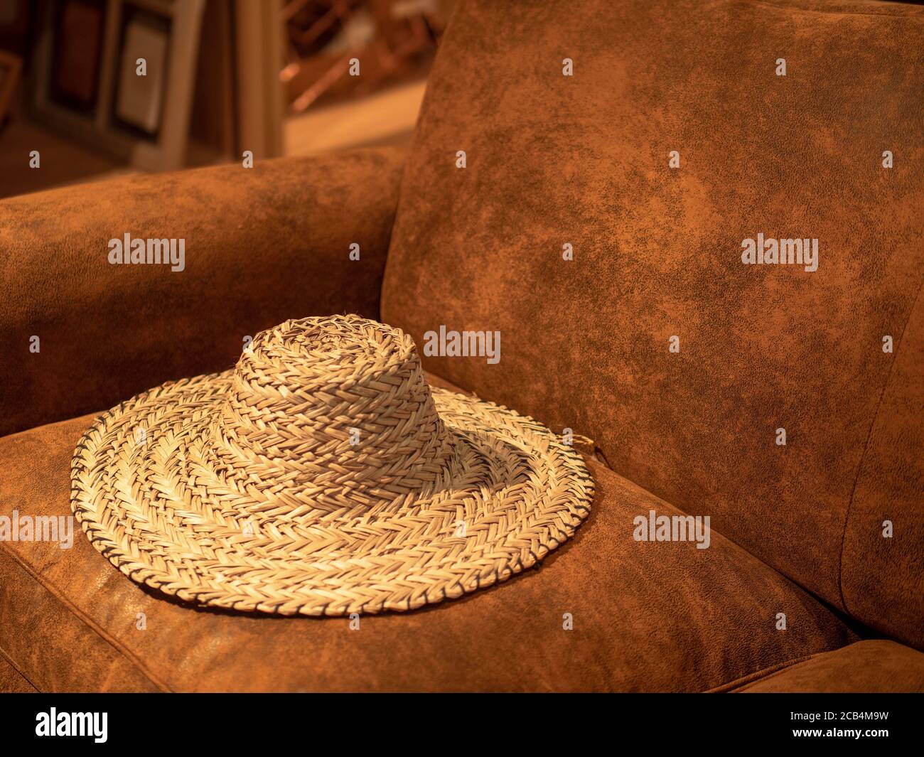 Gewebter Strohhut auf einem braunen Ledersofa Stockfoto