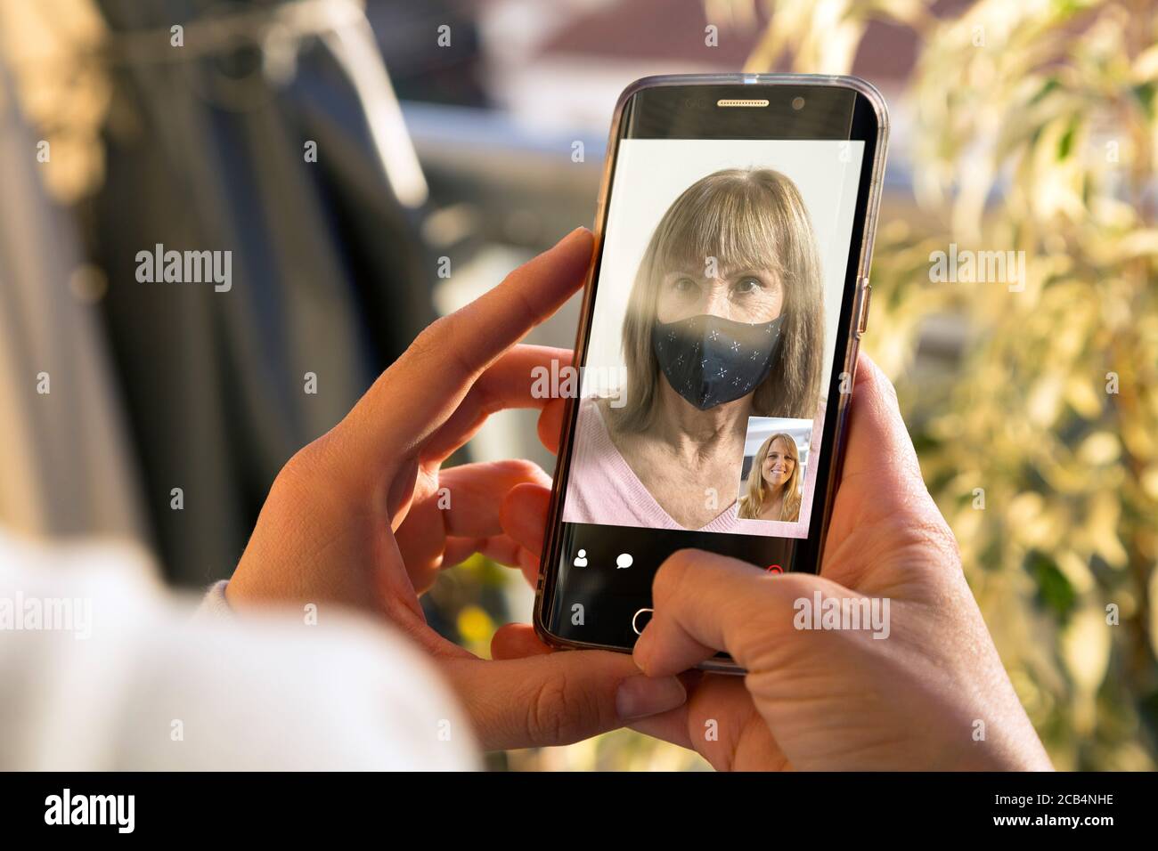 Zwei Frauen, die sich über einen Videoanruf auf einem Smartphone unterhalten. Ältere Frau mit medizinischer Maske mit einem Video-Chat mit einem Mädchen auf dem Handy. Stockfoto