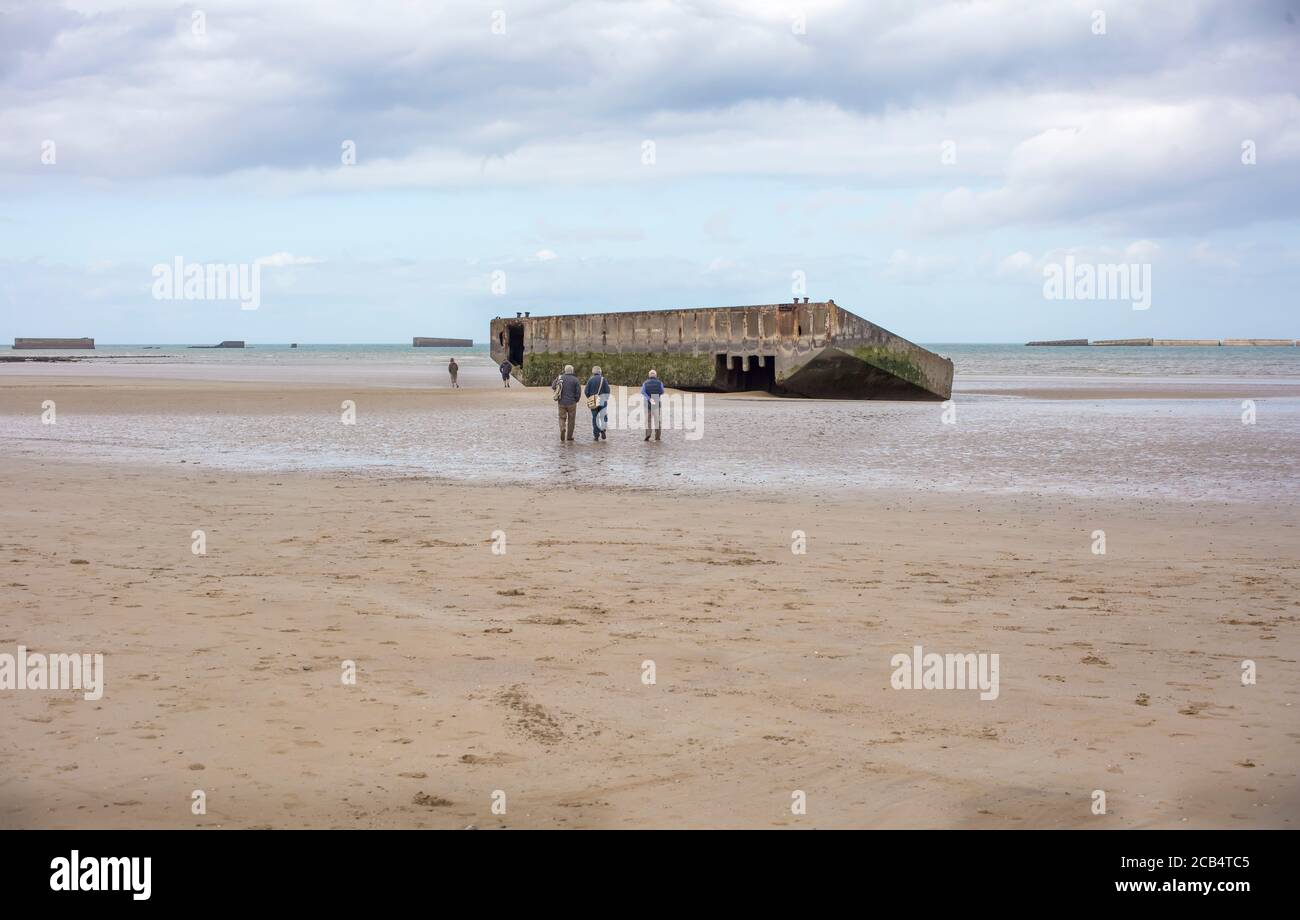 Männer am Strand schauen auf Überreste von Mulberry Häfen und blockieren Schiffe von D-Day Landungen in Arromanches-les-Bains, Normandie, Frankreich Stockfoto