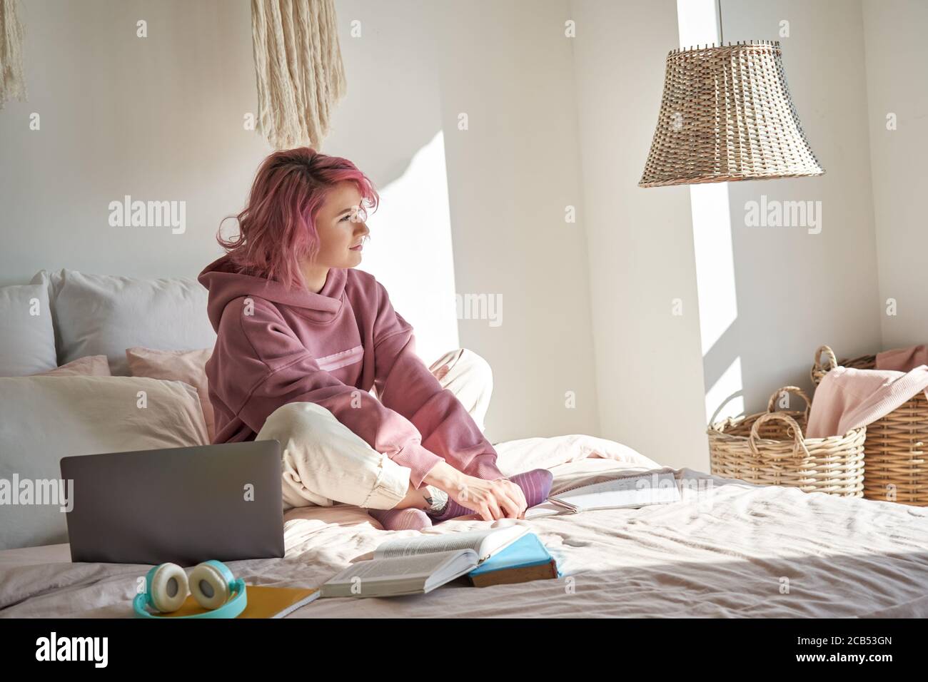 Verträumt teen Mädchen rosa Haare tragen Kapuzenpullover im Bett sitzen denken wegschauen. Stockfoto