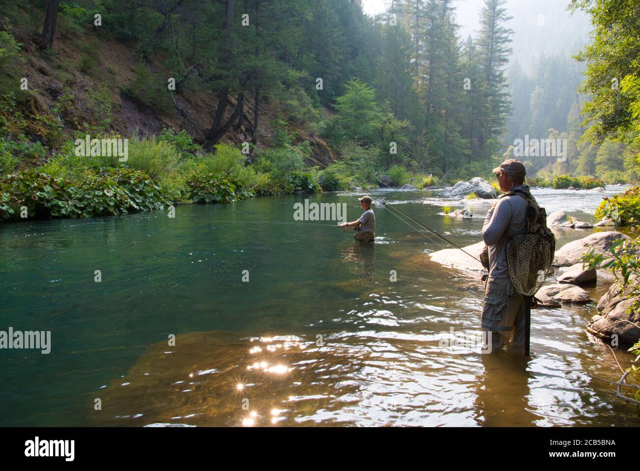 Menschliche Fliegenfischen im tiefen blauen Teich im Fluss mit Führung steht am Rand des Wassers mit Ausschaufeln NET und geben Sie Anweisungen Stockfoto