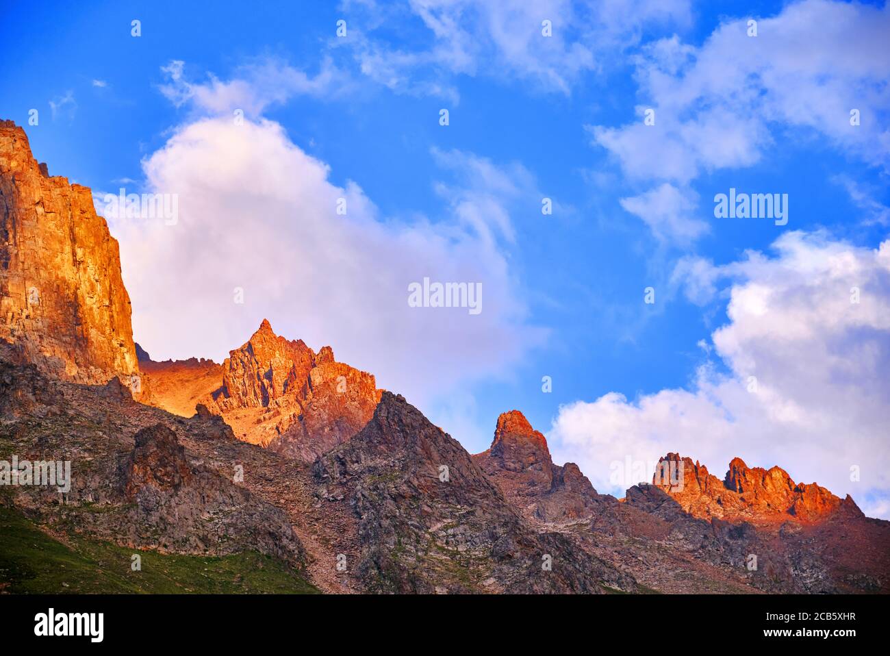 Riesige Klippen auf dem Hintergrund des blauen Himmels mit Wolken im Licht der untergehenden Sonne; majestätische Aussicht auf die Berge bei Sonnenuntergang Stockfoto