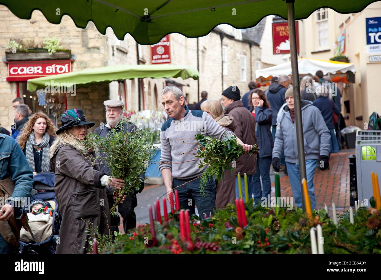 Eine Frau wählt Weihnachtsdekorationen von Stechpalme, Beeren auf einem Cotswold Bauernmarkt Stockfoto