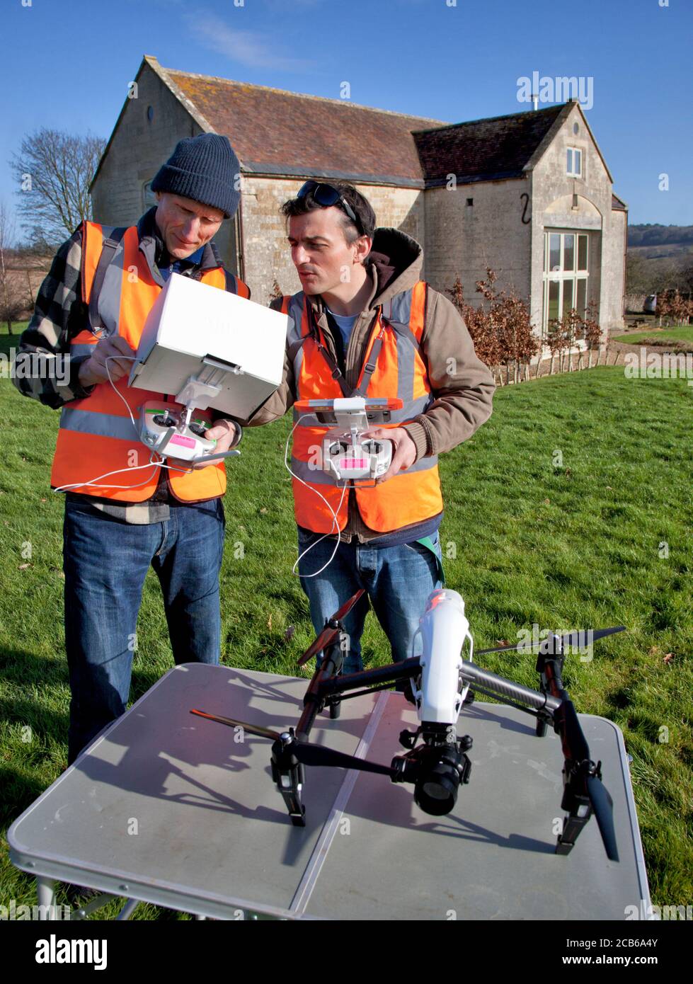 Zwei Männer bereiten sich darauf vor, eine Drohne mit einer Kamera zu fliegen Über einen privaten Garten und umgebaute Scheune in den Cotswolds Stockfoto