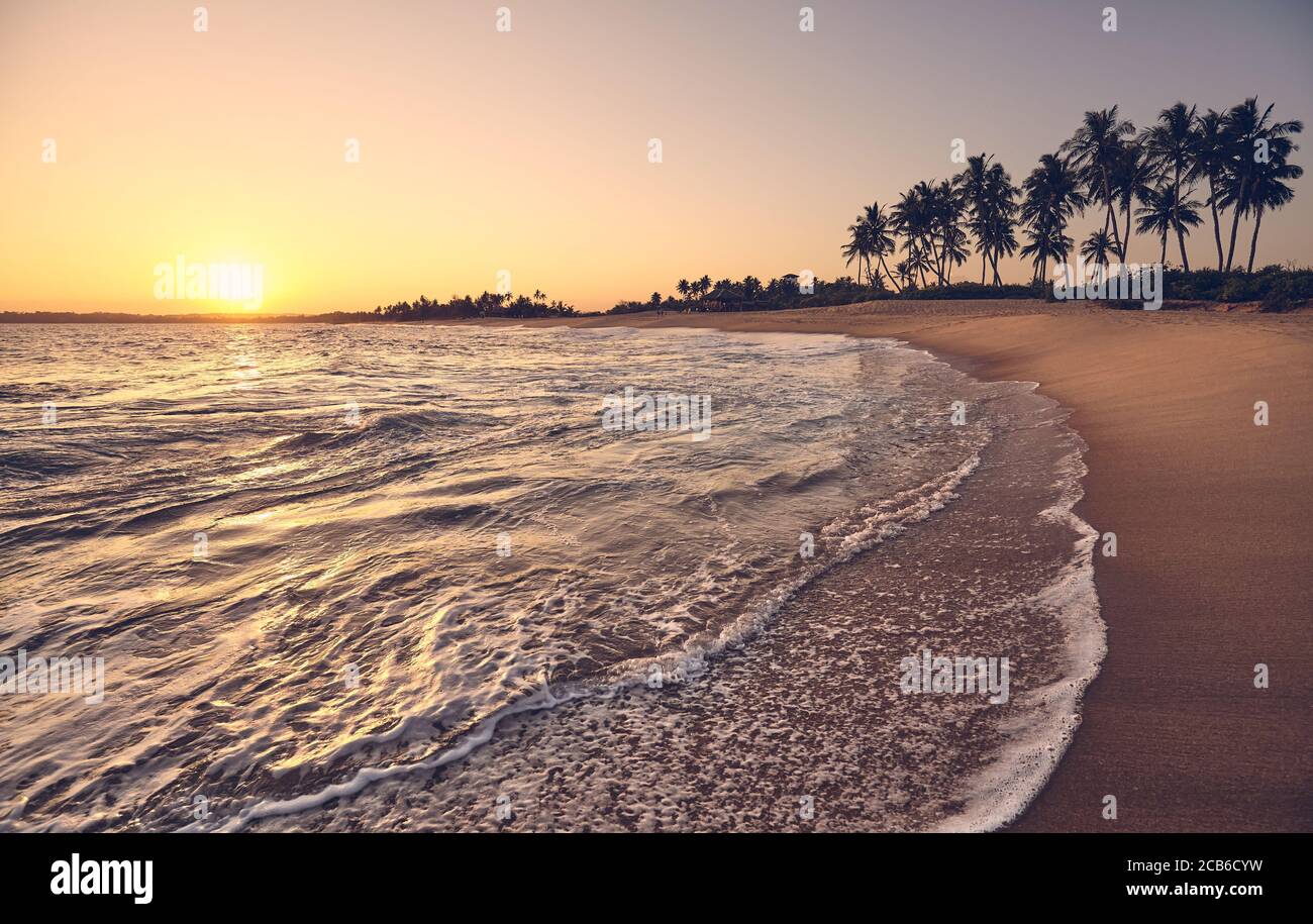 Tropischer Strand bei Sonnenuntergang mit Sonne im Wasser reflektiert, Farbtonung angewendet. Stockfoto