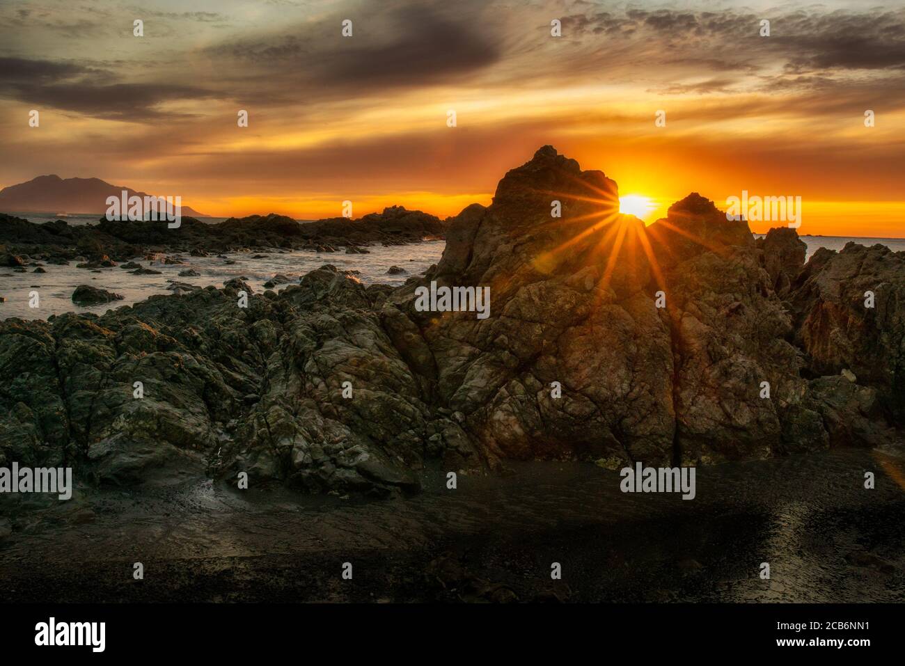 Spektakuläre Sonne Flare zwischen den Spalten in den Felsen bei Morgendämmerung an der Kaikoura Küste Stockfoto