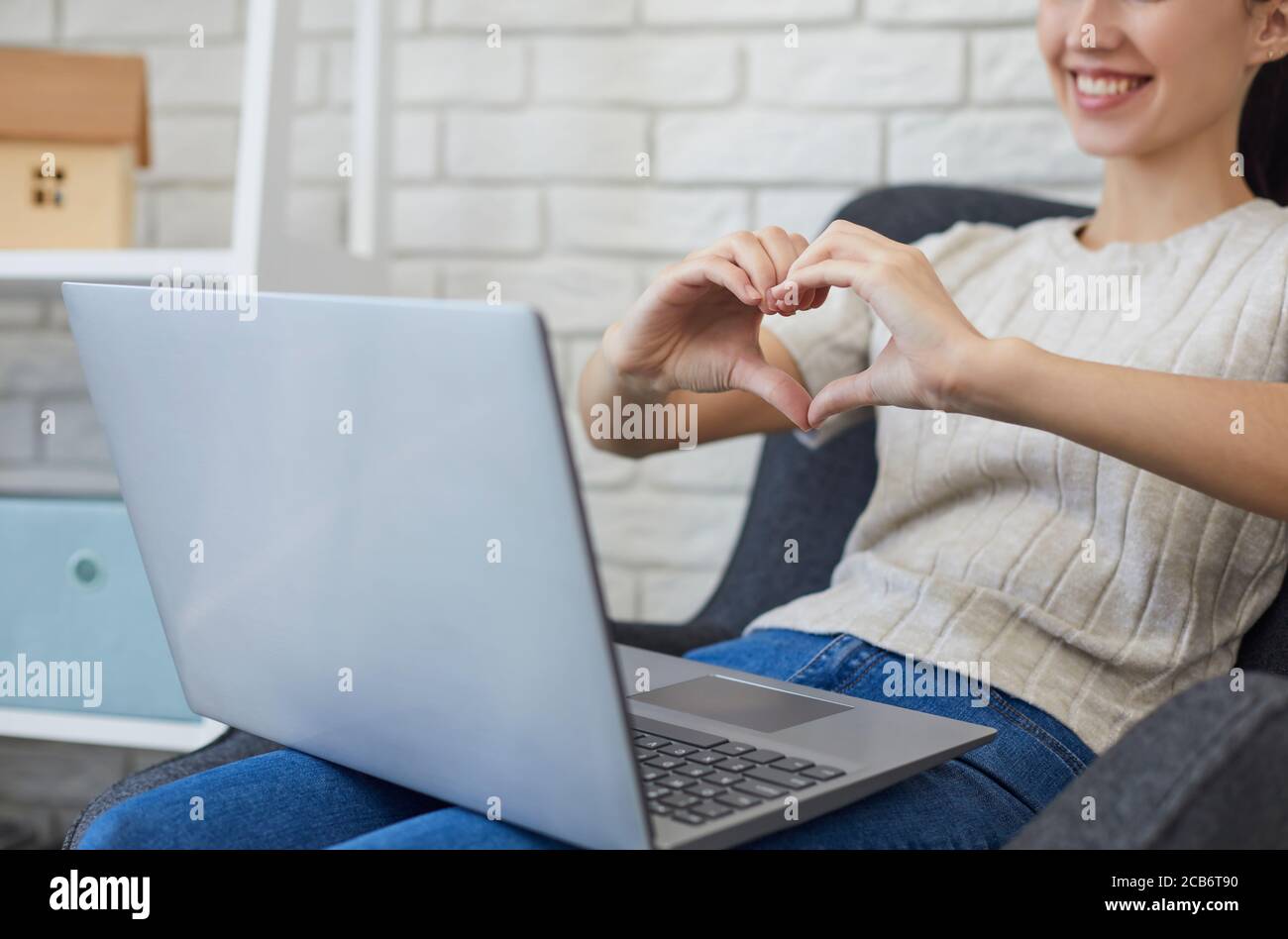 Online-Dating. Verkürzte Ansicht der jungen Frau zeigt Herz mit Händen zu ihrem Freund, während Online-Gespräch auf Laptop Stockfoto