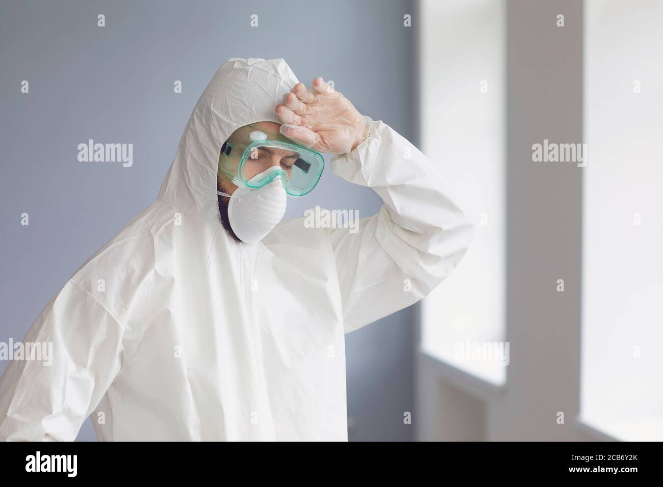 Erschöpfter Arzt in Schutzkleidung Hazmat Anzug Wischen Stirn in der Klinik. Medic arbeitet an viraler Epidemien Prävention in Innenräumen Stockfoto