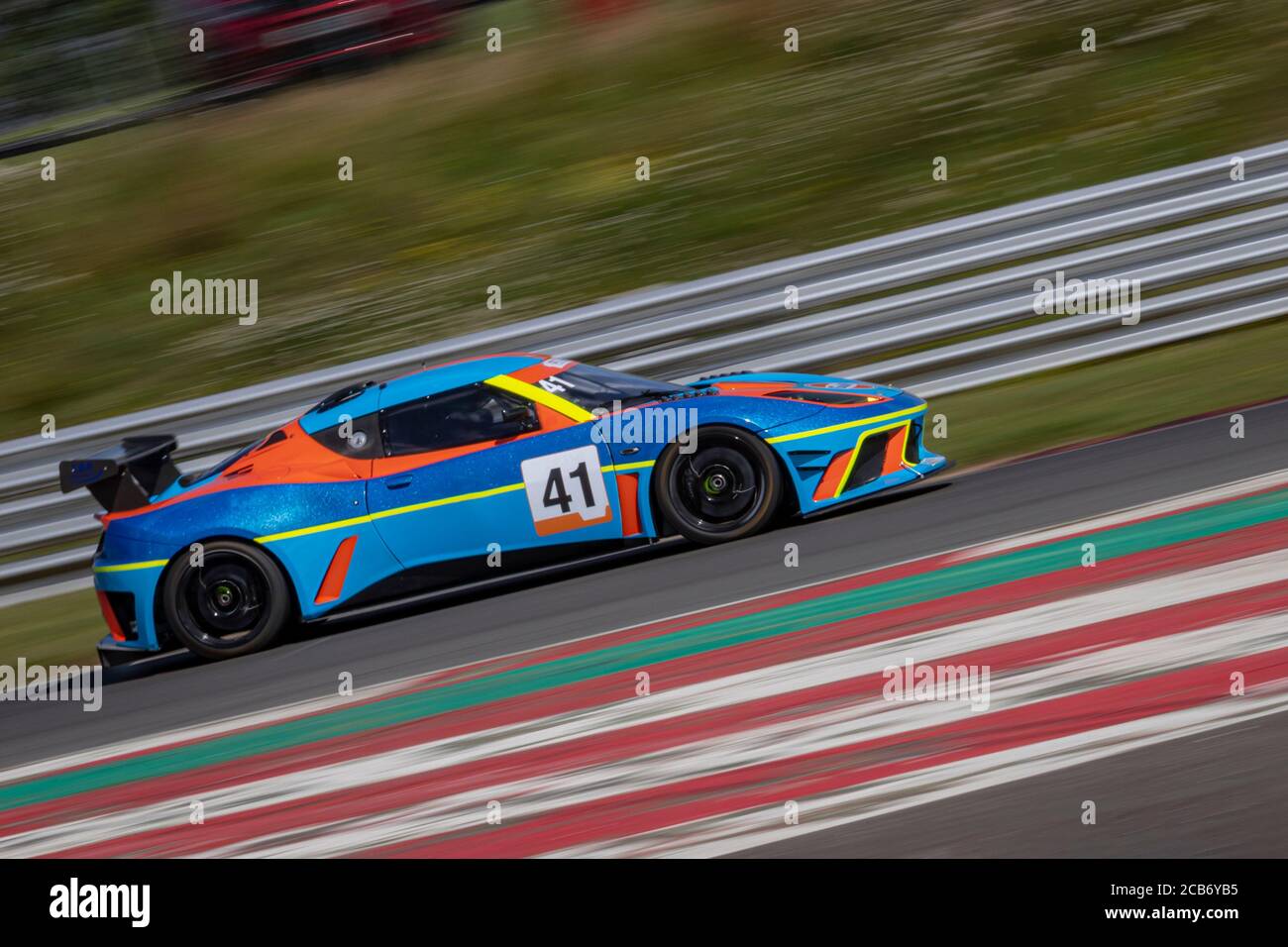 Eine Schwenkaufnahme eines blauen und orangenen Rennwagens, der eine Strecke fährt. Stockfoto