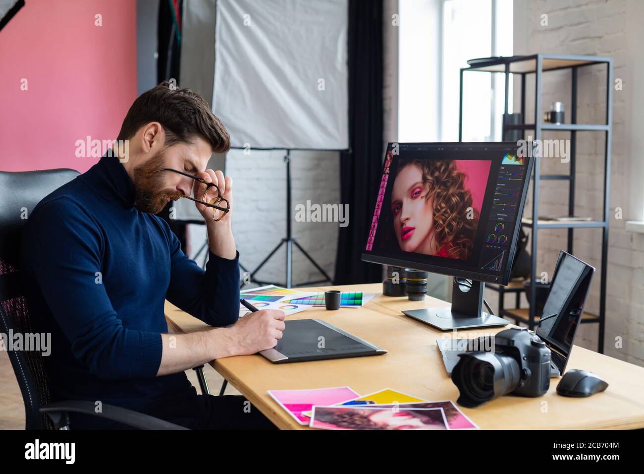 Porträt von müde Grafikdesigner arbeiten Überstunden im Büro. Gestresste Arbeiter haben Augenstrapazheitssymptome. Retoucher Arbeitsplatz im Fotostudio. Burnout Stockfoto