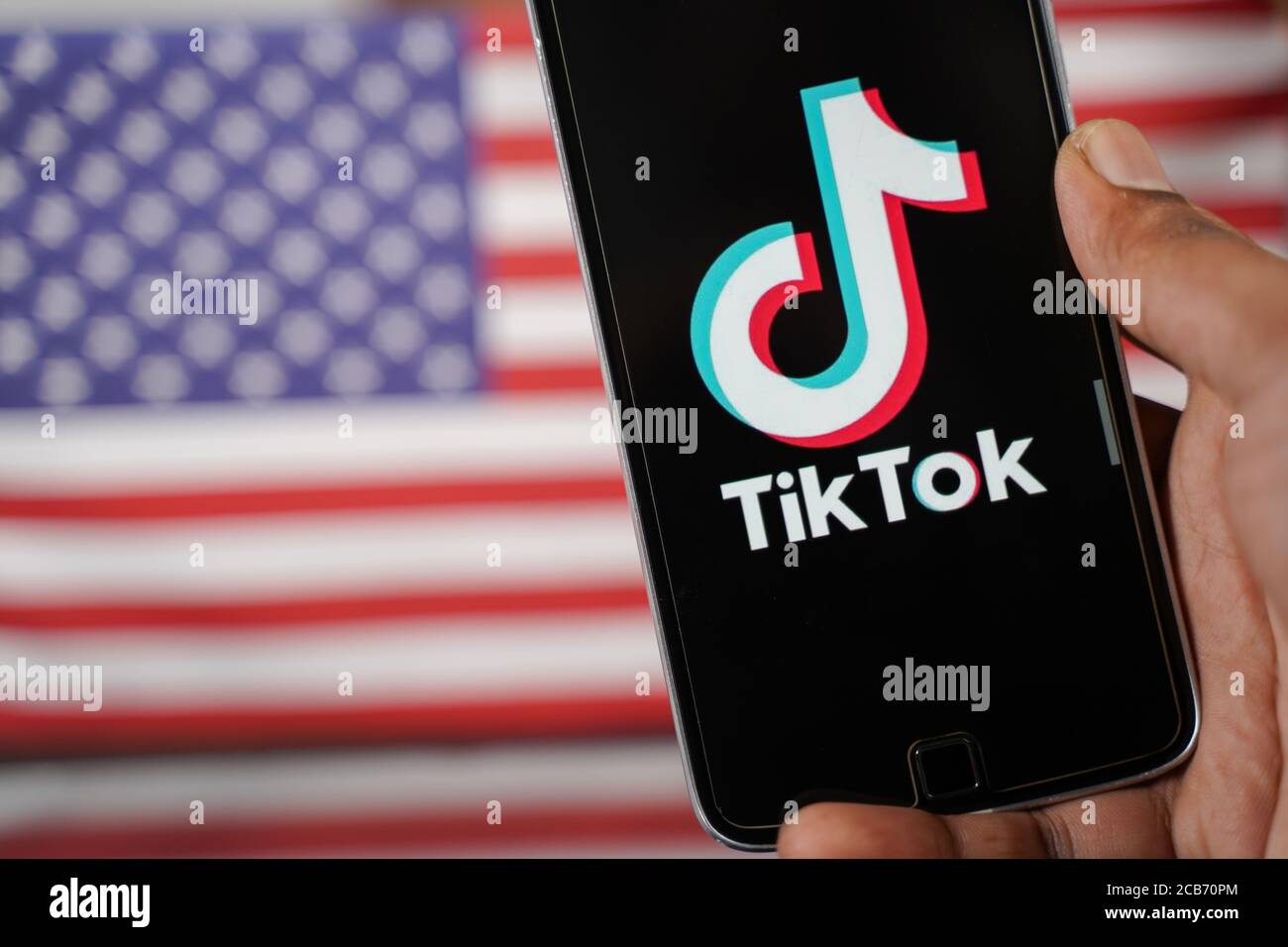 Maski, Indien - 4. August, 2020 : Nahaufnahme der Hände mit der tik tok App mit US- oder amerikanischer Flagge als Hintergrund und Kopierraum. Stockfoto