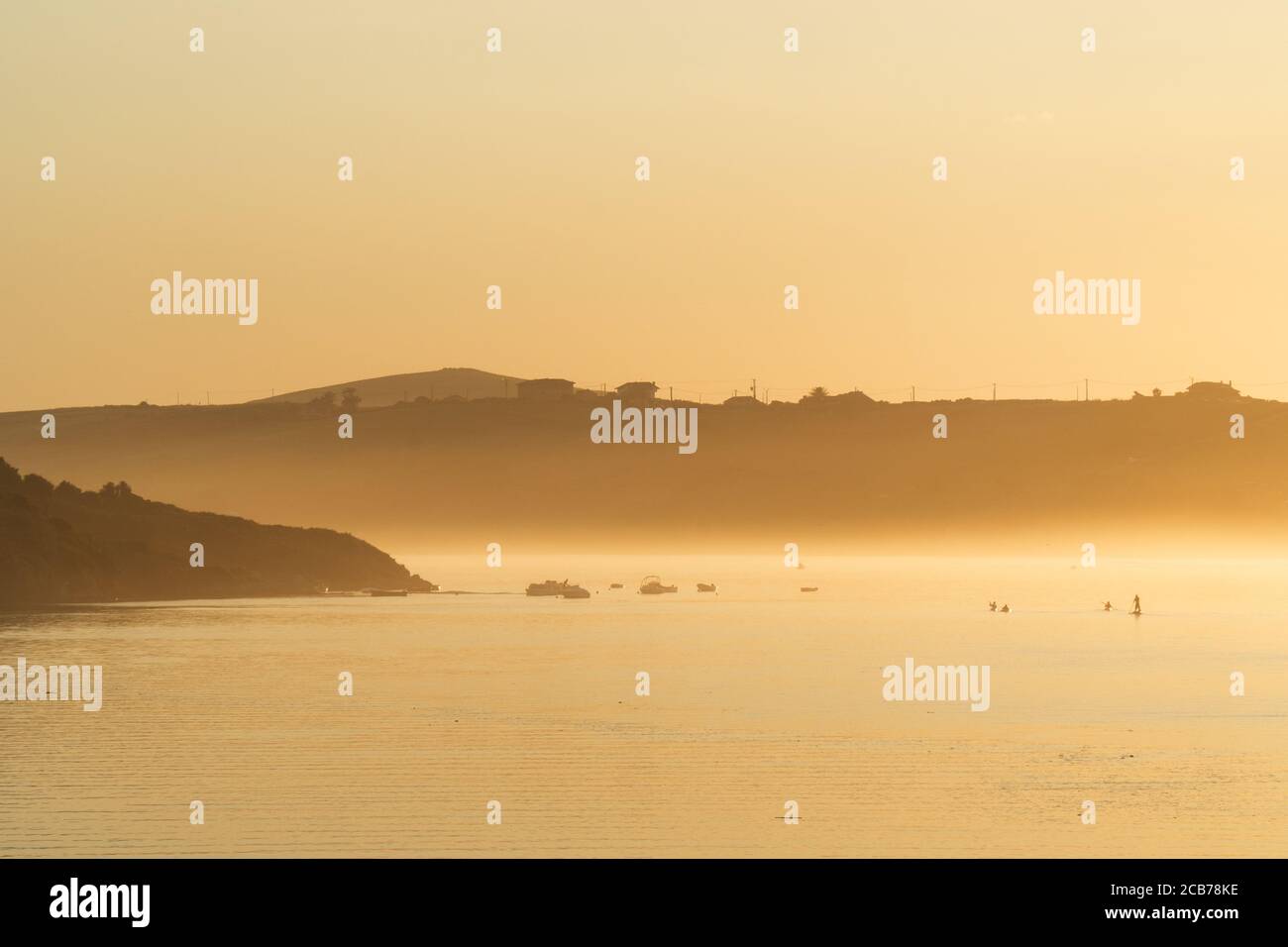 Blick auf den nebligen Fluss im Sonnenuntergang mit einigen Menschen üben Wassersport vor dem Ende des Tages Stockfoto