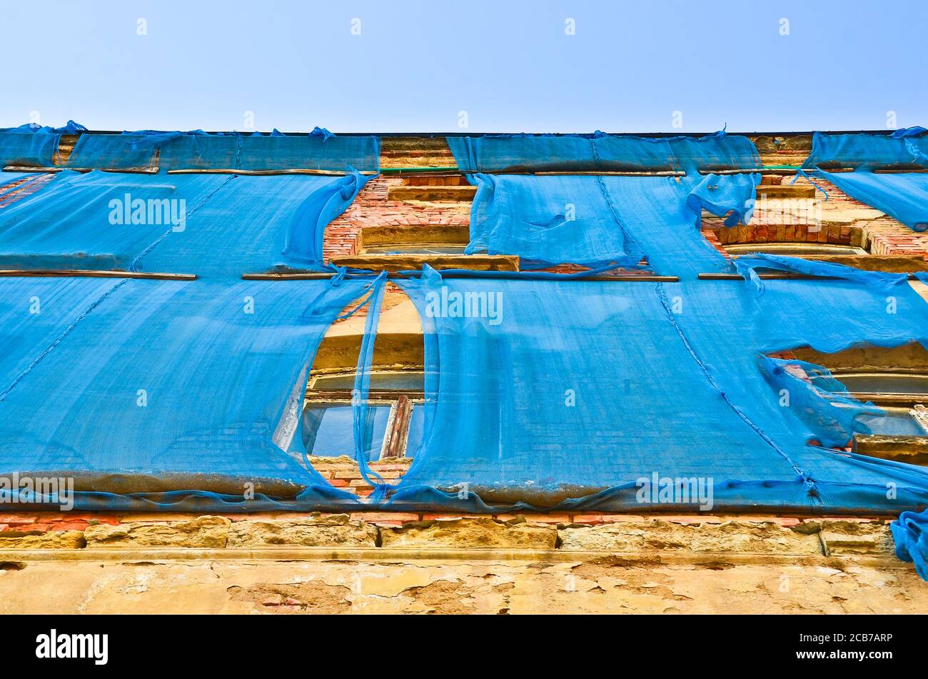 Die Fassade eines alten ruinösen Gebäudes ist mit verkrümmelt Einige blaue Vorhänge, um die Fußgänger zu schützen Stockfoto