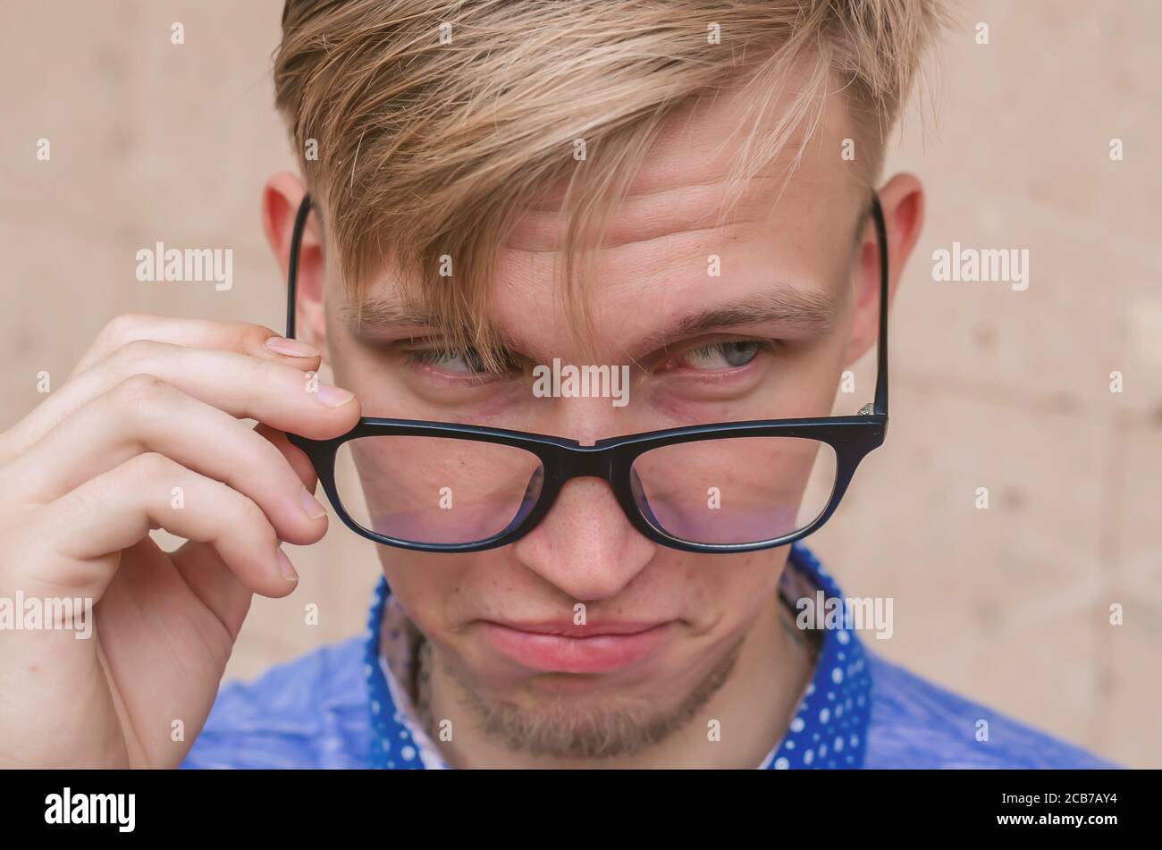 Blonde Mann mit kleinem Bart zieht seine Brille in Überraschung.Junge Mann mit lustigen Haarschnitt in der Brille Grimasse machen - lustige Gesicht. Emotionen und si Stockfoto