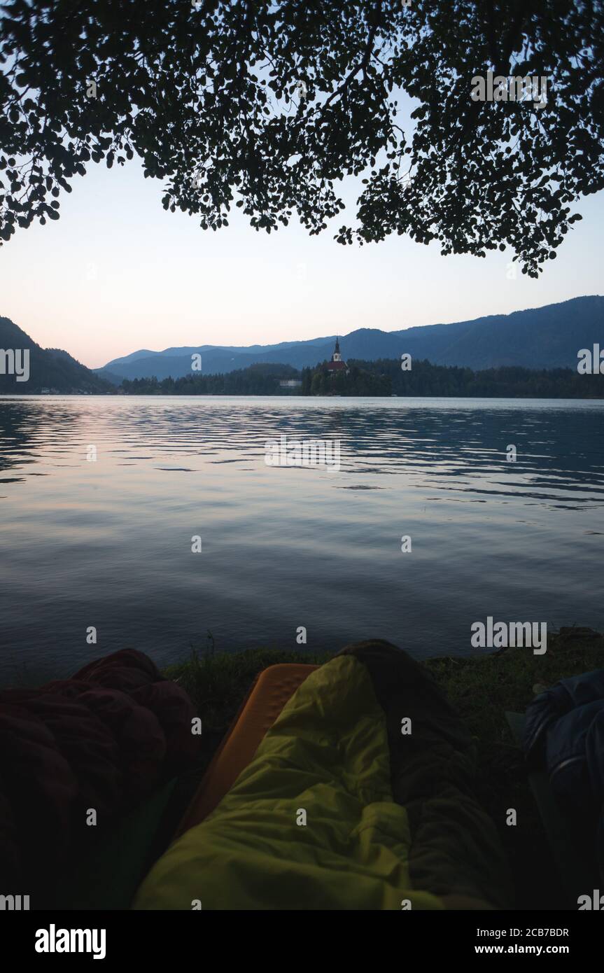Am frühen Morgen See Bled in Slowenien. Ruhiger See, aufgehende Sonne hinter den Bergen, Alpen. Schlafsäcke im Vordergrund, Outdoor-Abenteuer im Trigl Stockfoto