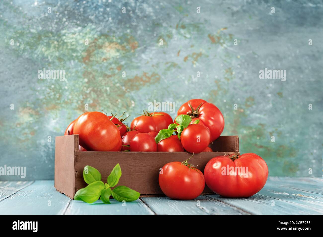 Frische und saftige Tomaten in einer Holzkiste auf Licht TürkisHintergrund Stockfoto