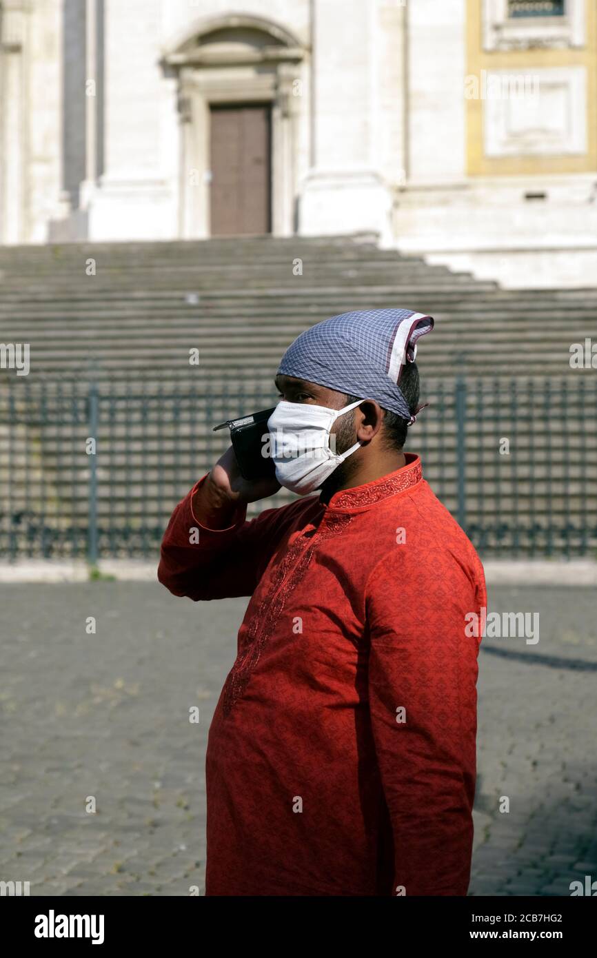 Asiatischer Mann, der eine medizinische Maske für das Covid 19 Coronavirus trägt und am Handy spricht. Rom zur Zeit des Covid 19, Italien, Europa, Europäische Union, EU. Stockfoto