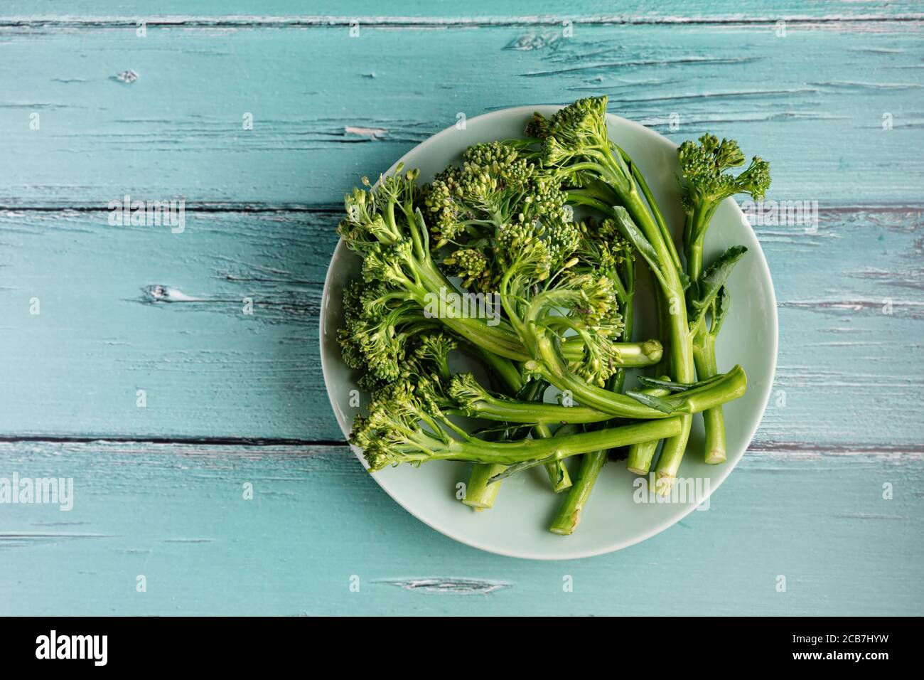 Draufsicht auf einen grünen Teller mit Broccolini auf rustikal Hellblauer Hintergrund Stockfoto