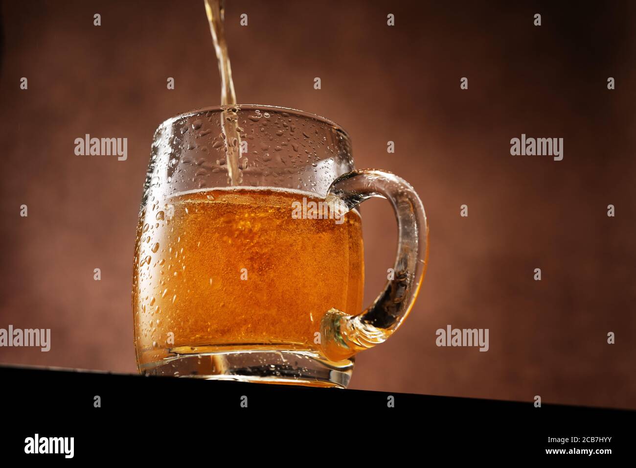 Leichtes Bier wird in einen Becher gegossen, der gegen Braun steht Hintergrund unter der Augenlinie Stockfoto