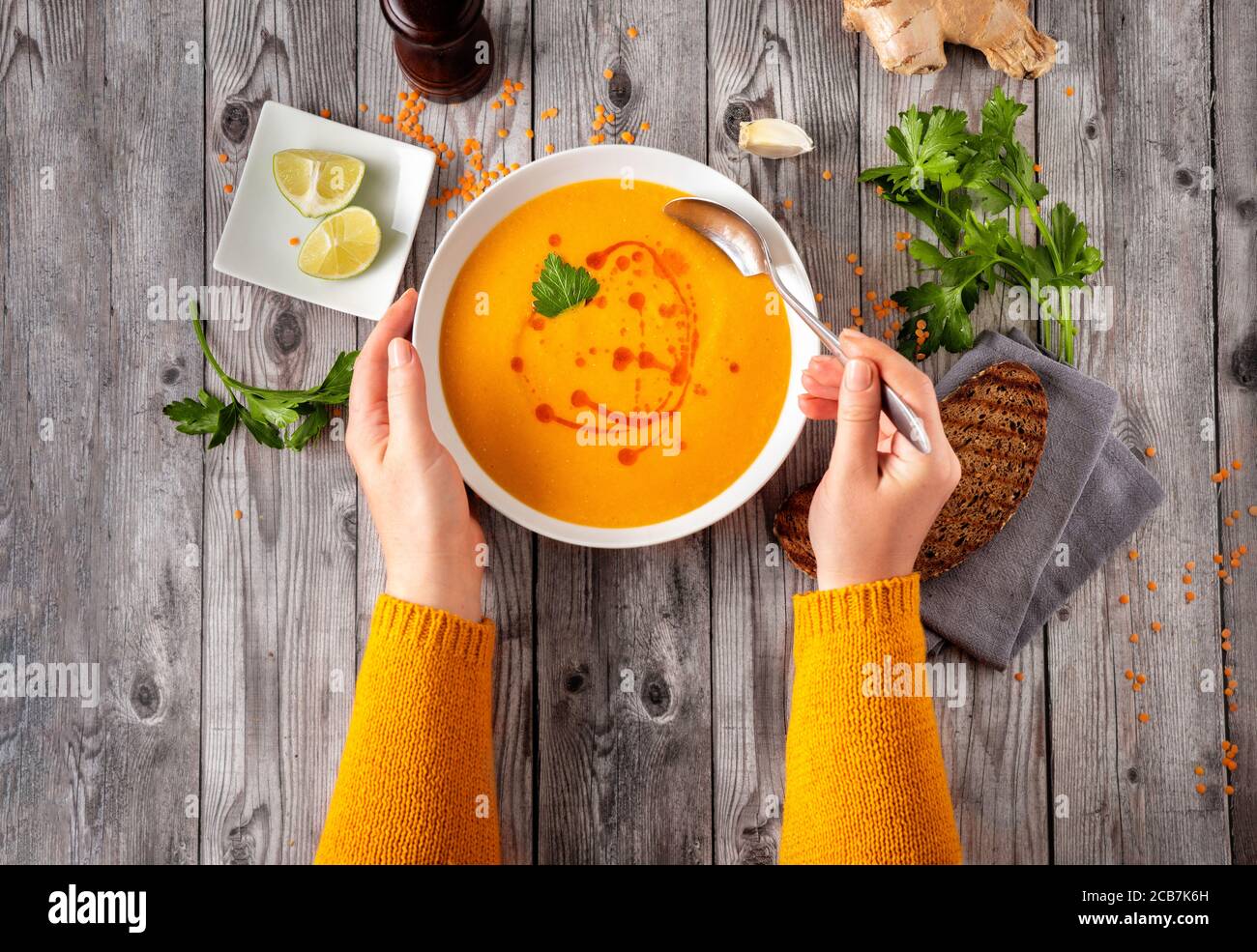 Draufsicht auf unkenntlich Frau in orange Pullover essen warm Und würzige Winterlinsensuppe Stockfoto