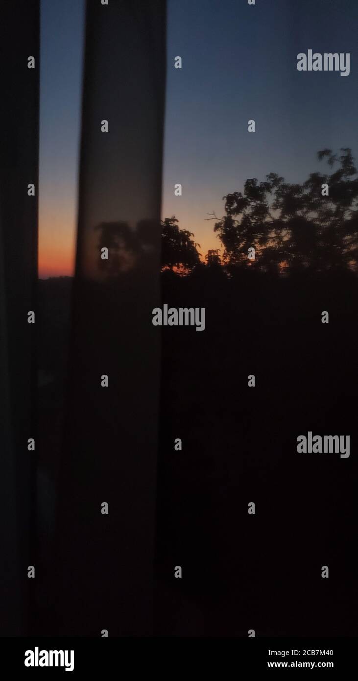 Verwischen Sie abstrakte Ansichten von Sonnenaufgang in der Dunkelheit mit Baumsilhouetten. Künstlerischer Film Korn Effekt durch Tüll Vorhang geschossen Stockfoto