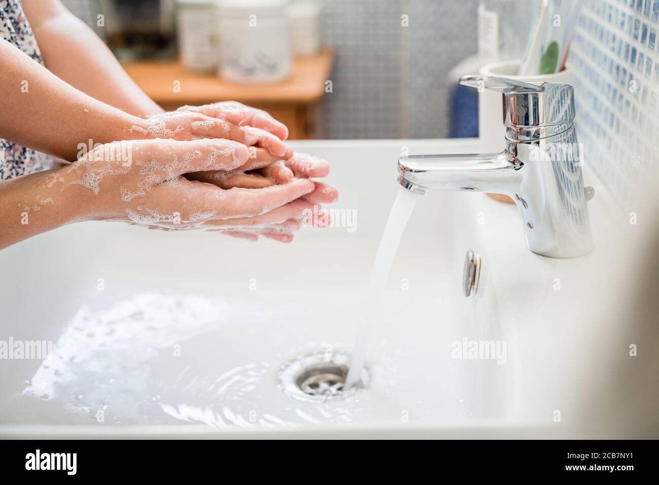 Mutter und Mädchen Kind waschen Hände zusammen im Bad Waschbecken mit viel Seife unter fließendem Wasserhahn. Seitenansicht Stockfoto