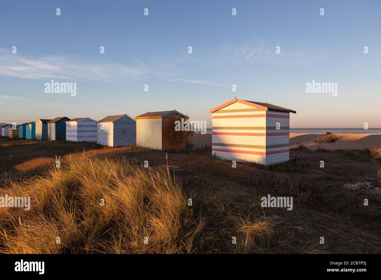 Die untergehende Sonne trifft auf die Rückseite von einigen englischen Strandhütten an einem Strand in Kent. Stockfoto Die untergehende Sonne trifft auf die Rückseite von einigen englischen Strandhütten an einem Strand in Kent. Stockfoto