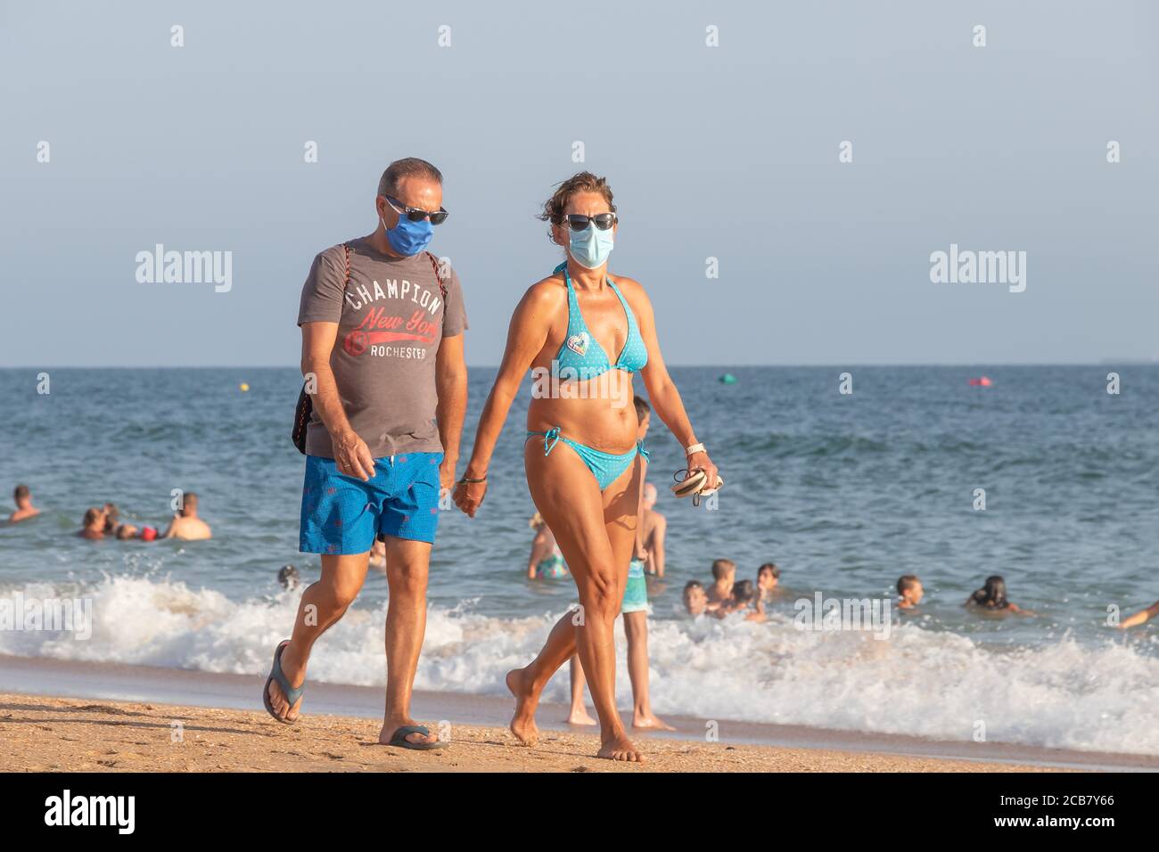 Punta Umbria, Huelva, Spanien - 7. August 2020: Paar, das am Strand entlang geht und Schutzmasken oder medizinische Gesichtsmasken trägt. Neue Normalität in Spanien mit sozialen di Stockfoto