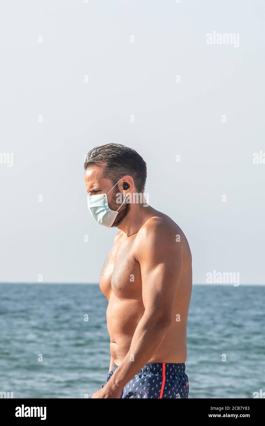 Punta Umbria, Huelva, Spanien - 7. August 2020: Frau, die am Strand entlang geht und Schutzmasken oder medizinische Gesichtsmasken trägt. Neue Normalität in Spanien mit sozialen DIS Stockfoto