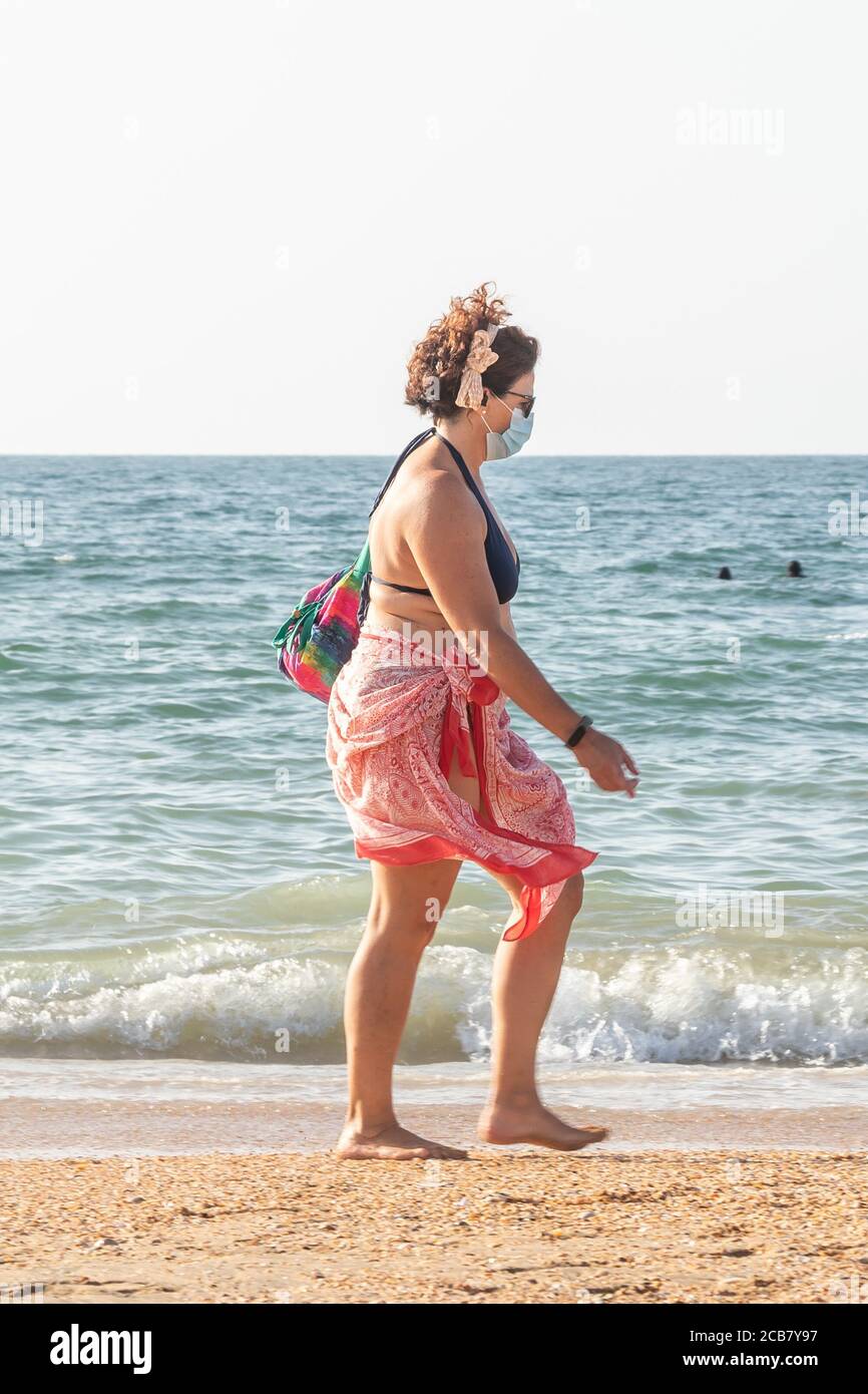 Punta Umbria, Huelva, Spanien - 7. August 2020: Frau, die am Strand entlang geht und Schutzmasken oder medizinische Gesichtsmasken trägt. Neue Normalität in Spanien mit sozialen DIS Stockfoto