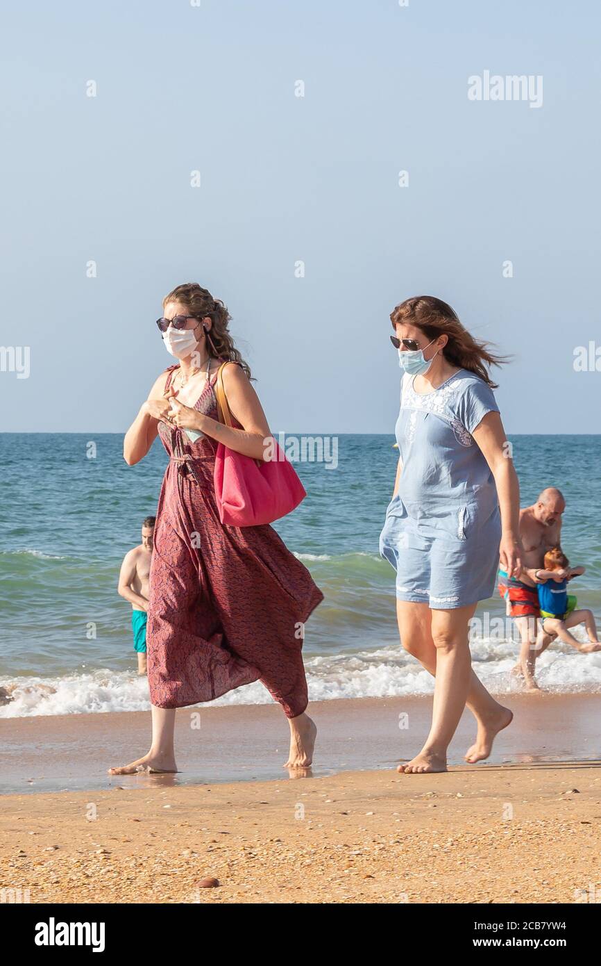 Punta Umbria, Huelva, Spanien - 7. August 2020: Zwei Frauen, die am Strand spazieren gehen und Schutzmasken oder medizinische Gesichtsmasken tragen. Neue Normalität in Spanien mit sozialen Stockfoto