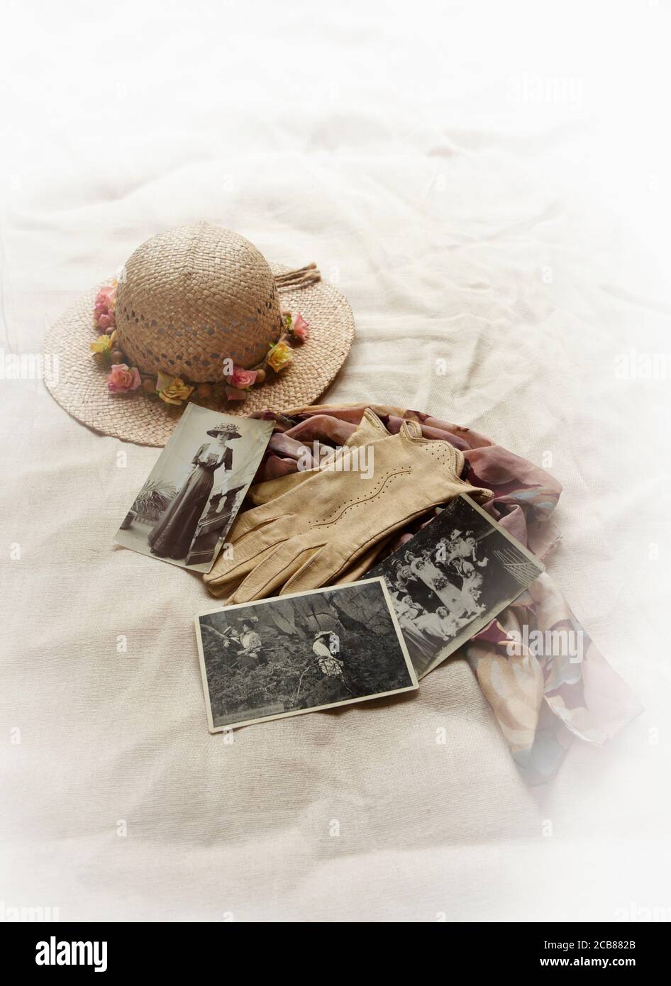 Strohhut mit Blumen am Rand mit Schal, Handschuhen und alten Fotografien Stockfoto
