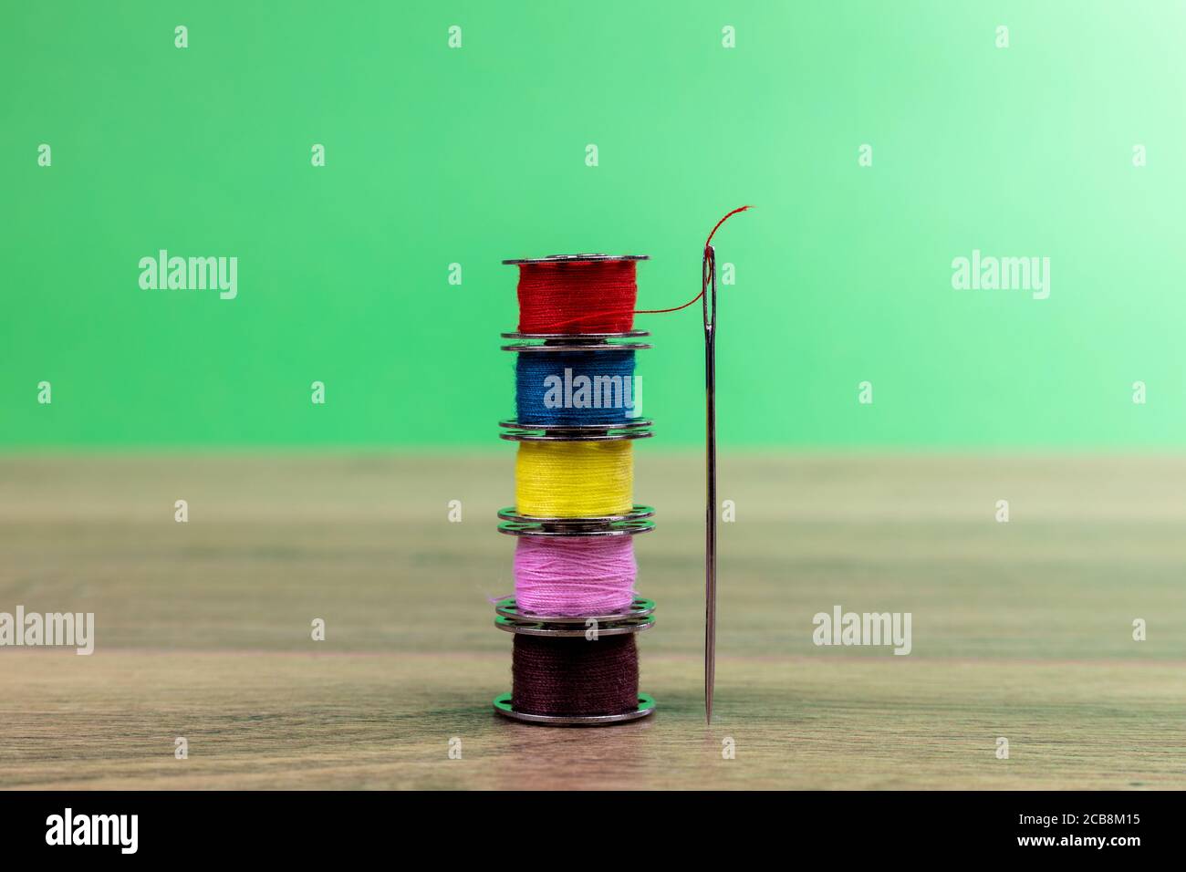 Spulen aus farbigem Baumwollfaden mit vertikaler Nadel mit grün Hintergrund Stockfoto