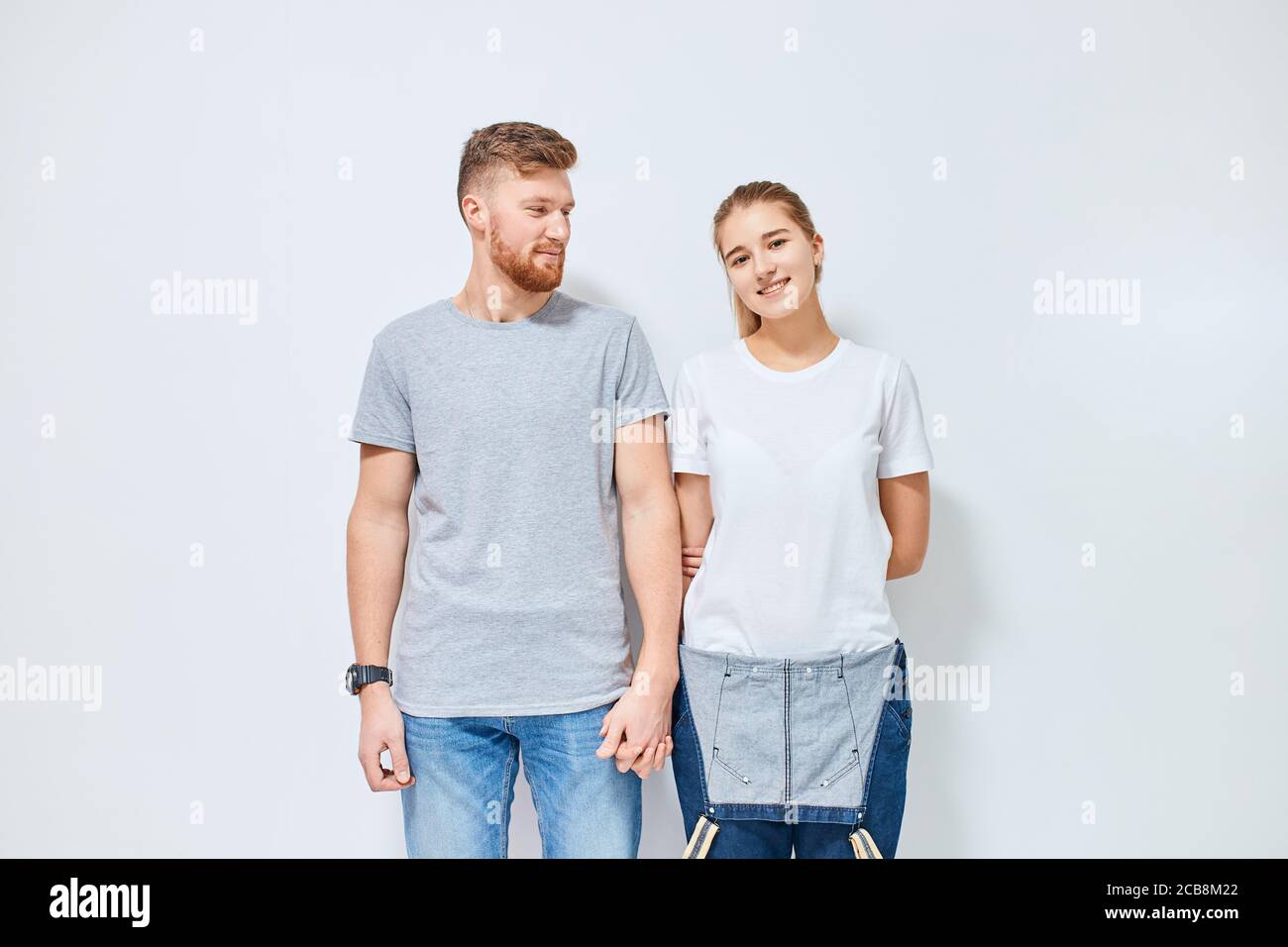 Nette junge glücklich Paar in der Liebe lächelnd Hände halten Blick auf Kamera, isoliert auf weißem Hintergrund Stockfoto