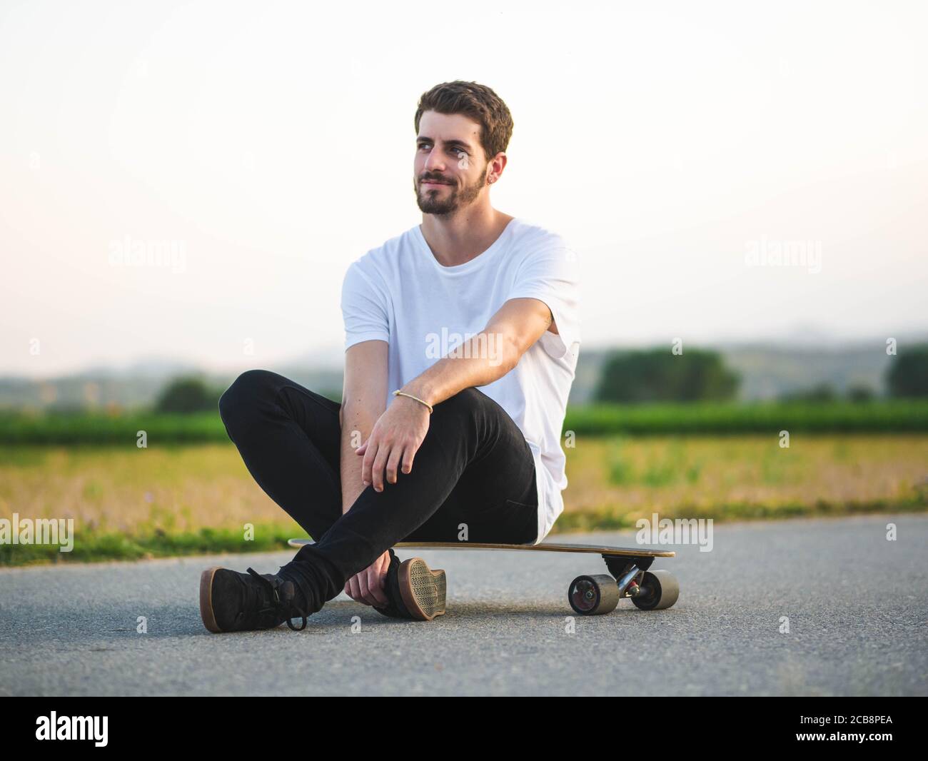 Shallow Focus Aufnahme eines jungen hübschen männlichen Sitzes Ein Skateboard Stockfoto