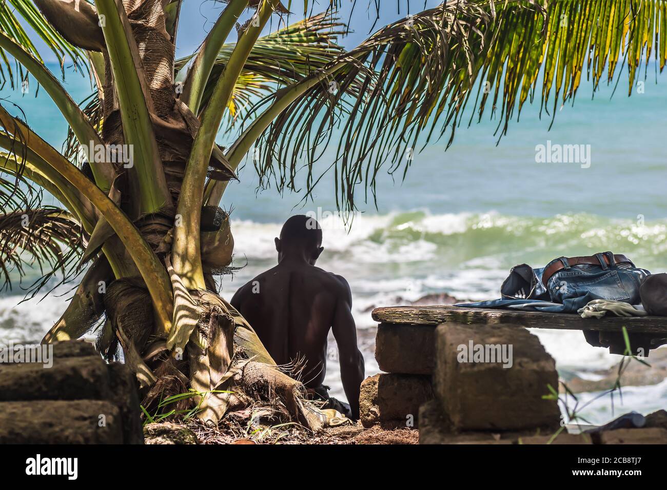 Afrika Mann sitzt am Meer in Axim Ghana. Jeans Hosen sind auf der Bank. Stockfoto