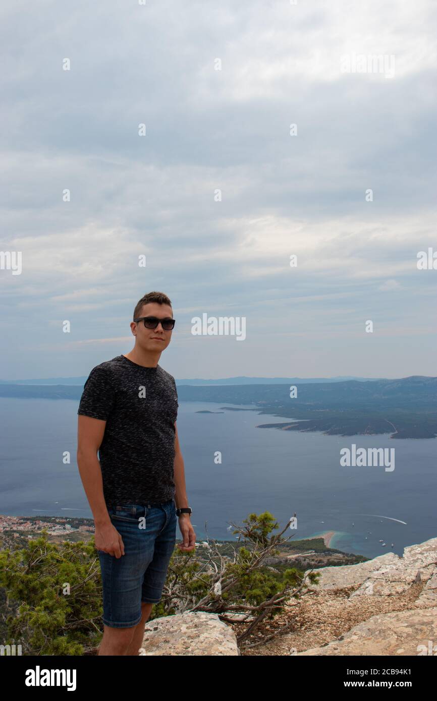 Vertikale Aufnahme eines jungen erwachsenen Mannes, der auf dem Berg Vidova gora, dem höchsten Punkt der Insel Brac, posiert. Beliebter Ort für Touristen, um pH-wert zu nehmen Stockfoto